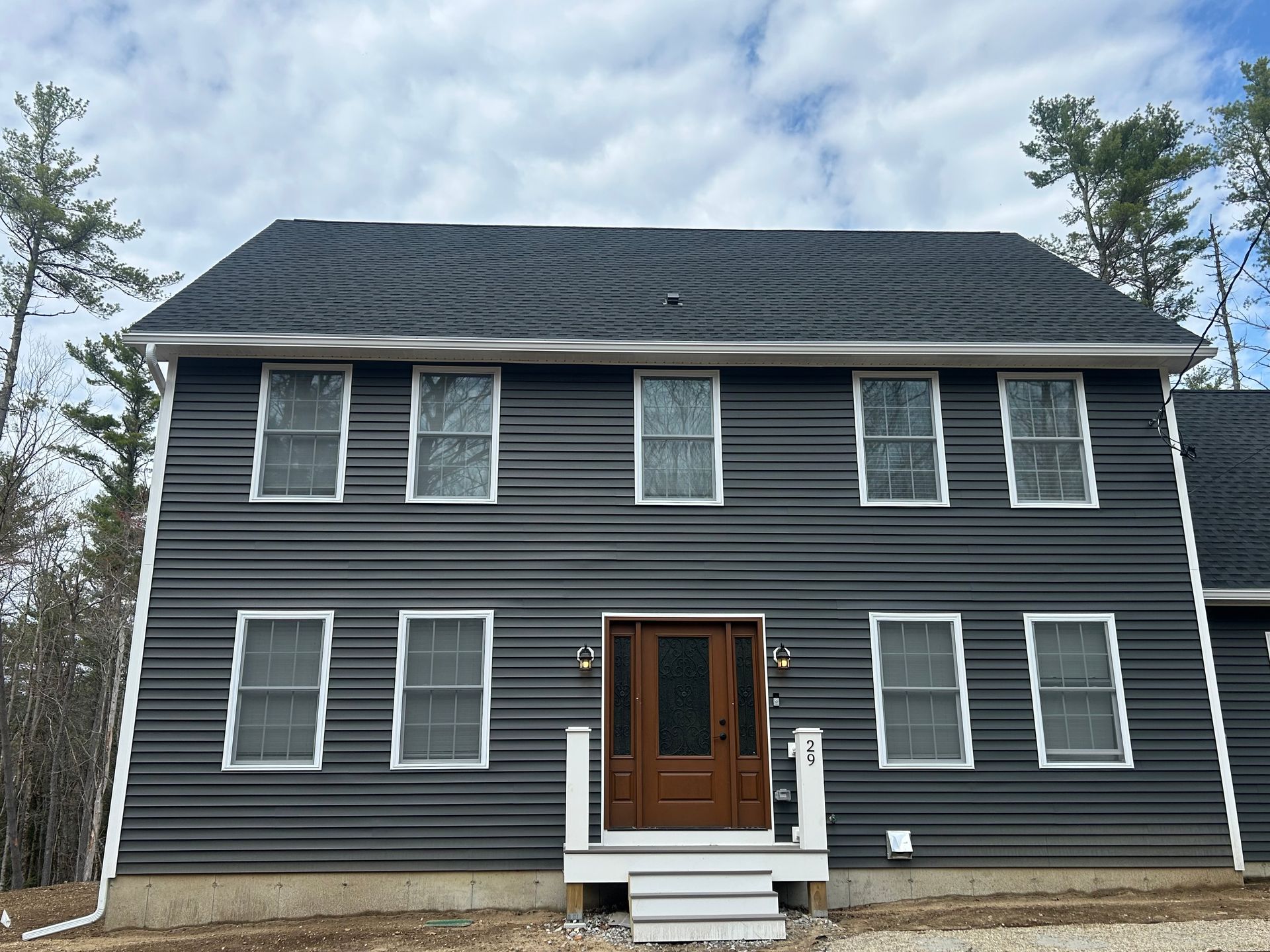 Two-story dark gray house with white trim and a wooden front door, seen from the front.
