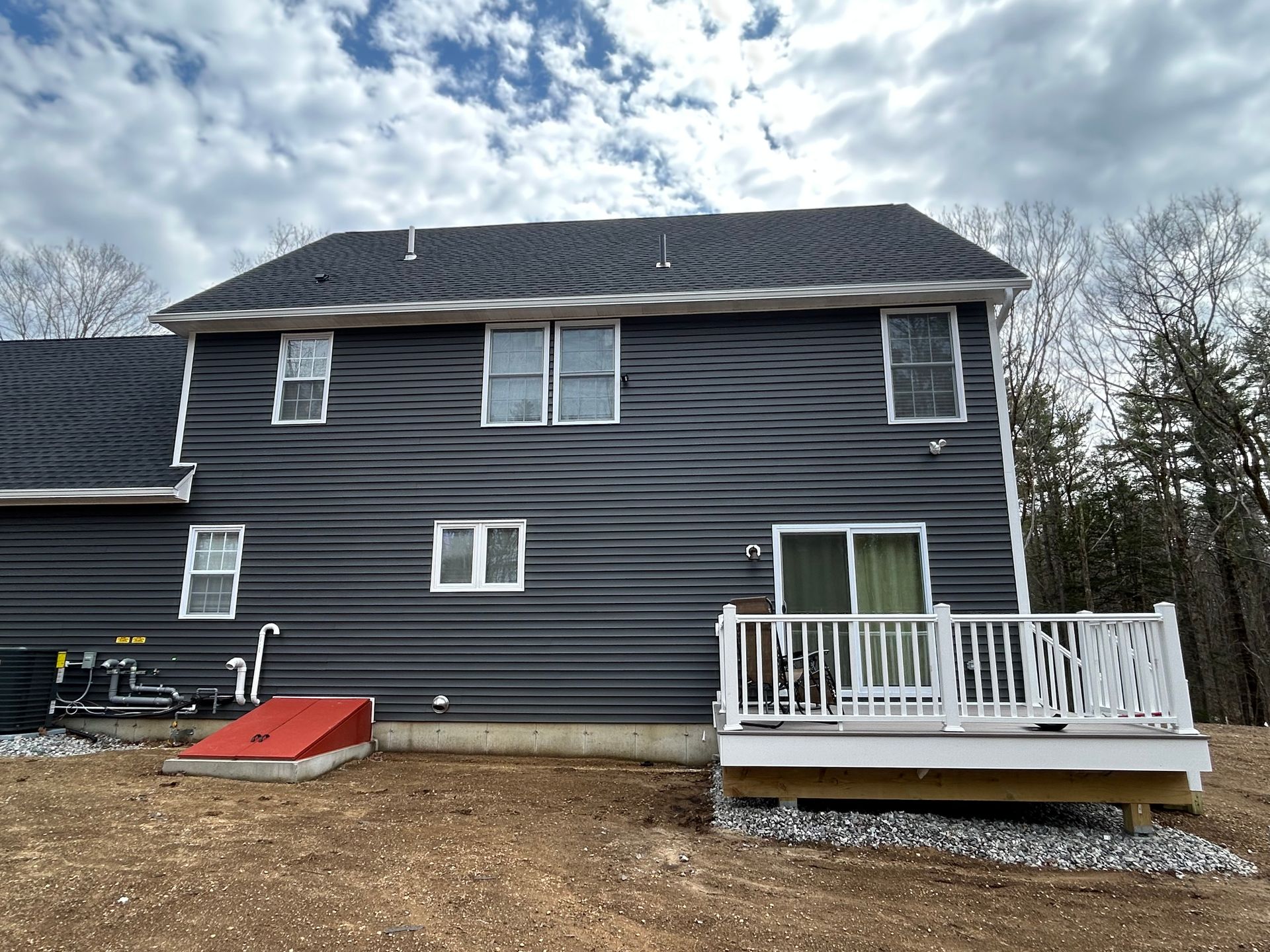 Dark blue two-story house with a small white deck and cloudy sky overhead