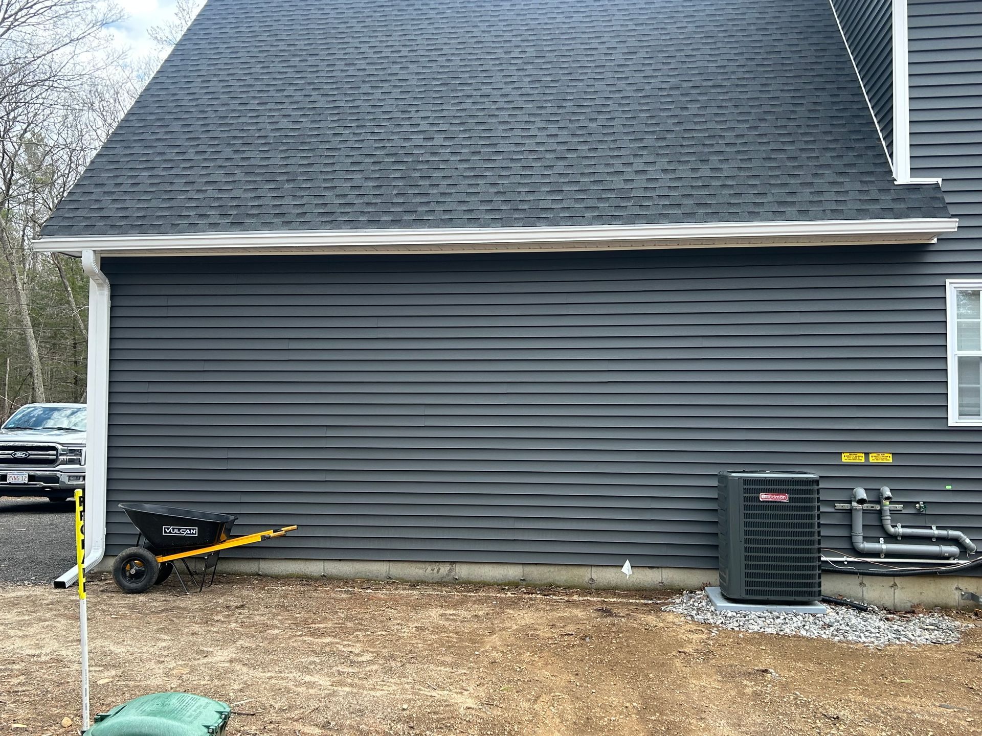 Gray house side wall with HVAC unit, black utility cart, and gravel along the foundation