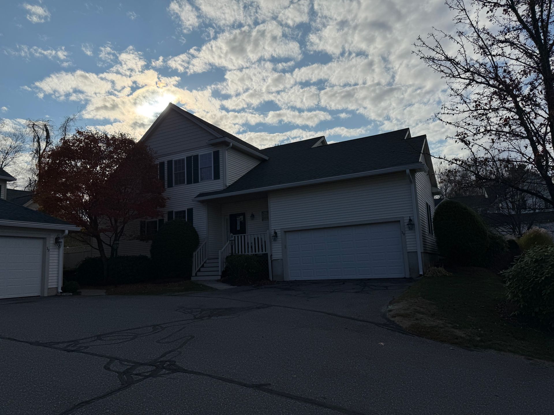 Suburban house with garage at dusk, silhouetted against a cloudy sky and driveway in front