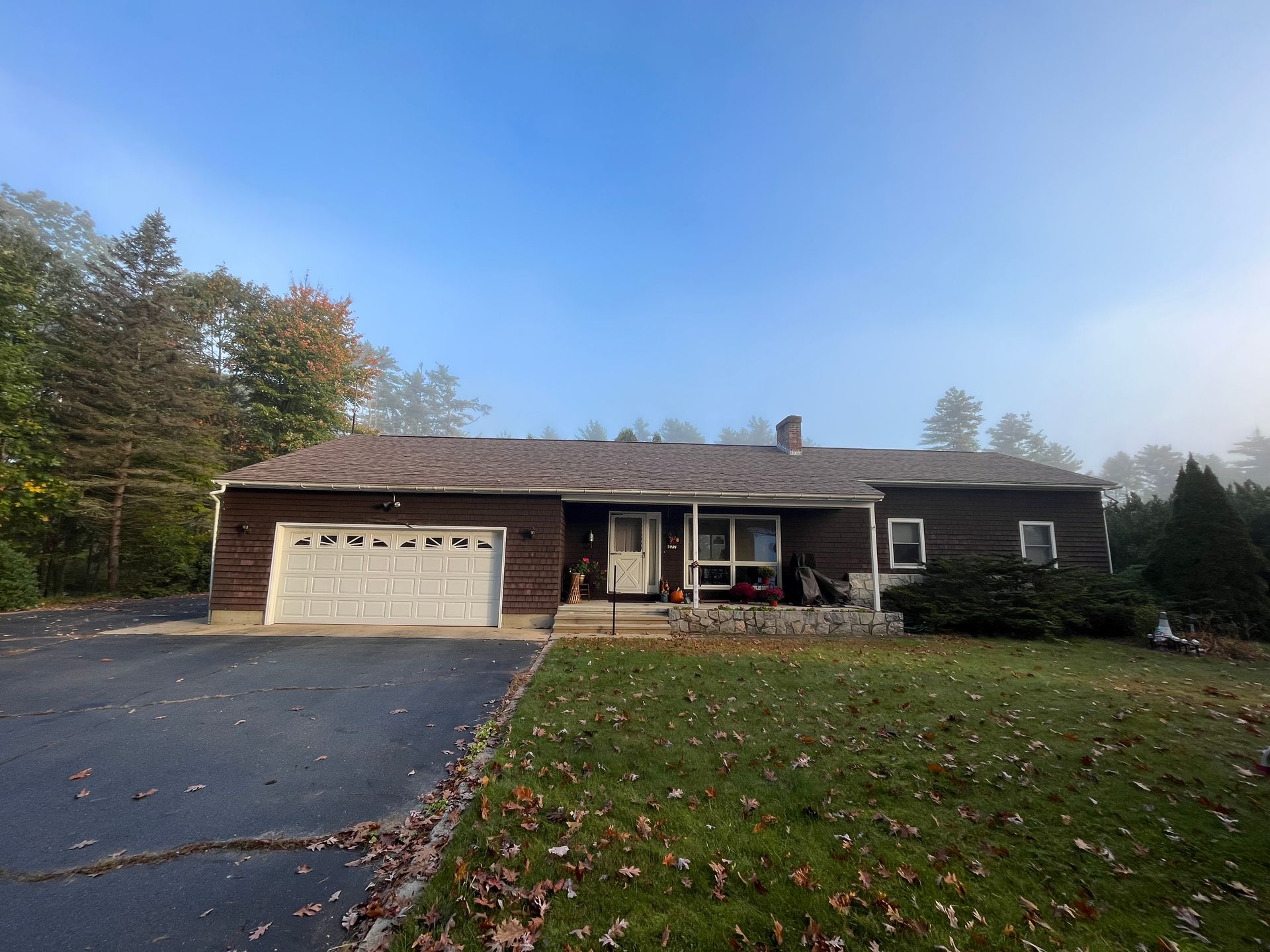 Single-story house with attached garage, dark roof, paved driveway, and front lawn under a clear sky