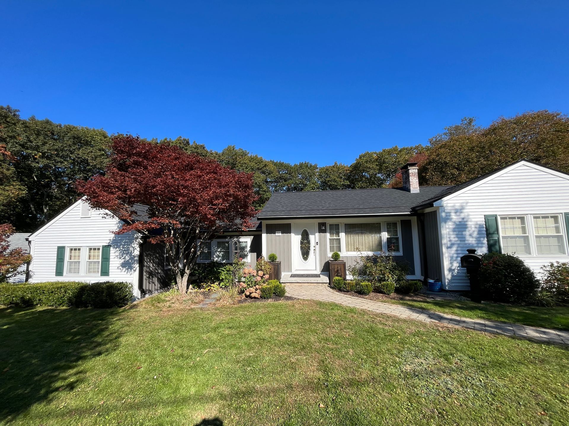 Single-story white house with a front lawn, walkway, and trees under a clear blue sky
