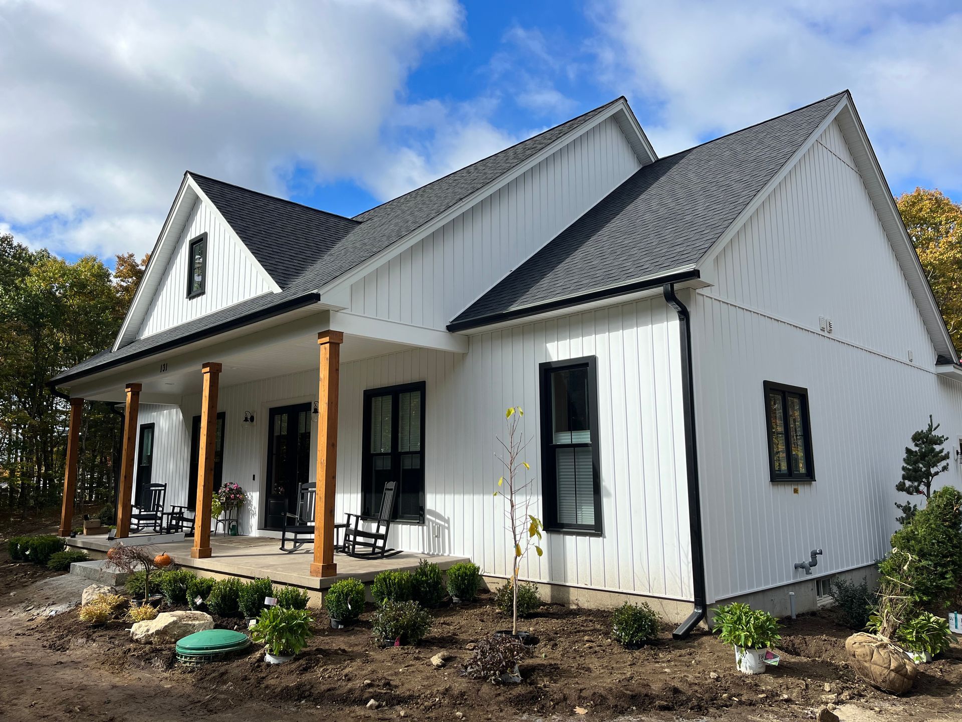 White farmhouse with gray roof and porch, set in a landscaped yard under a blue sky