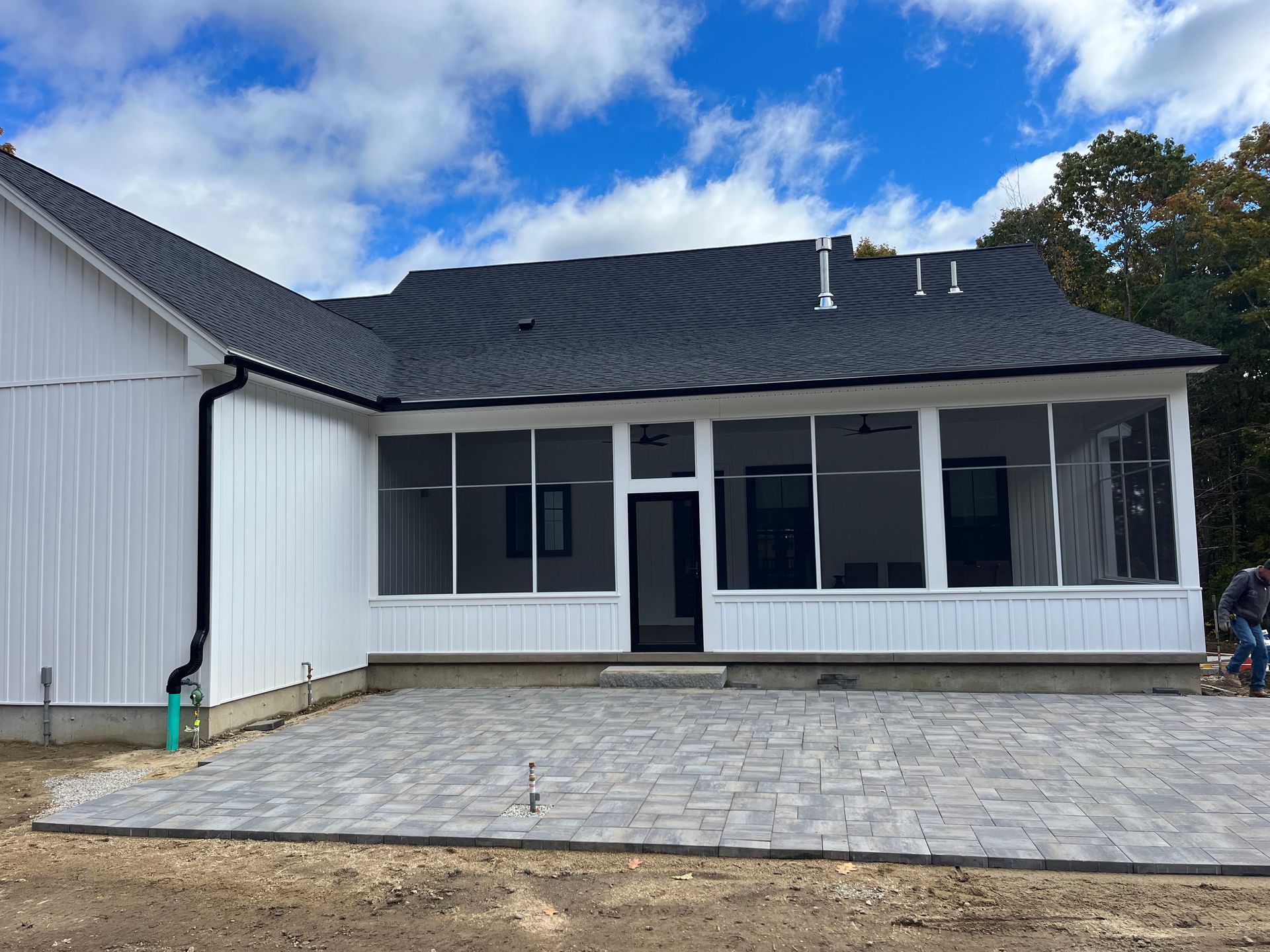 White house exterior with a dark roof, screened porch, and stone patio under a blue sky