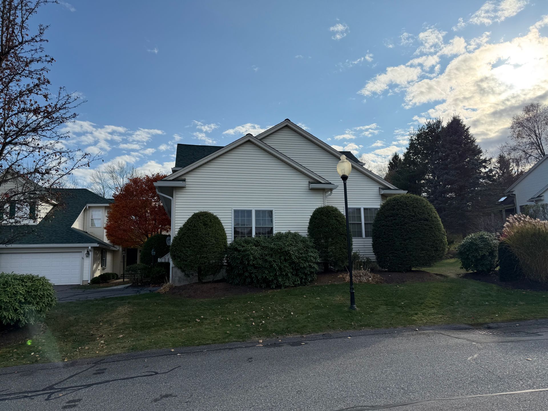 Suburban house with white siding, trimmed shrubs, and a garage under a partly cloudy sky