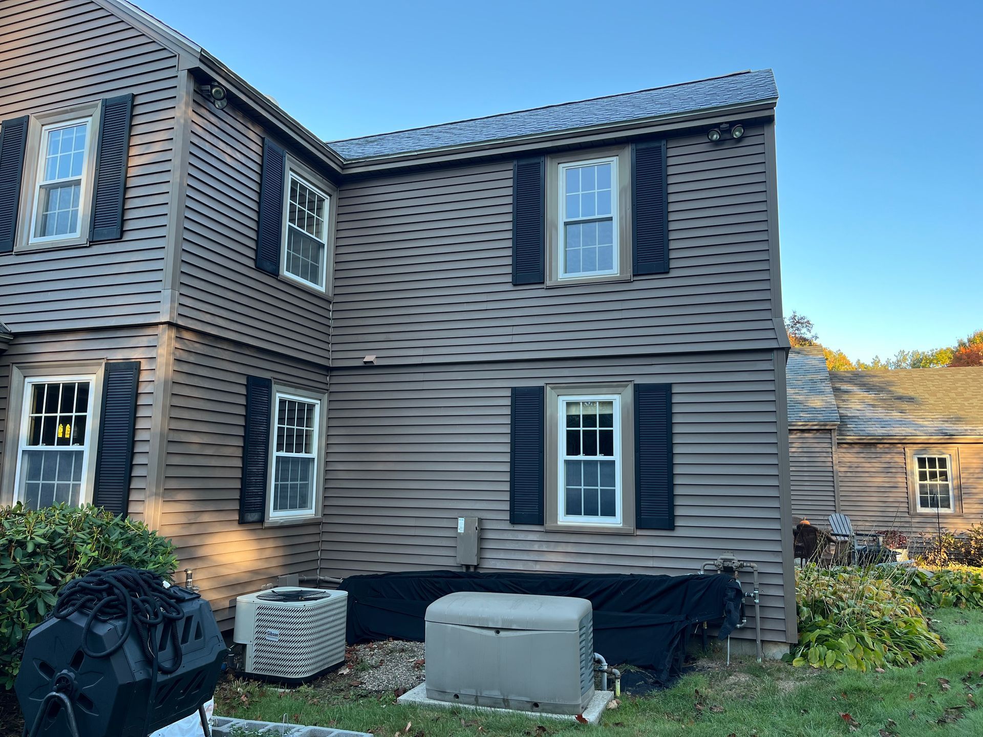 Exterior of a two-story gray house with white-trimmed windows and HVAC units in the yard