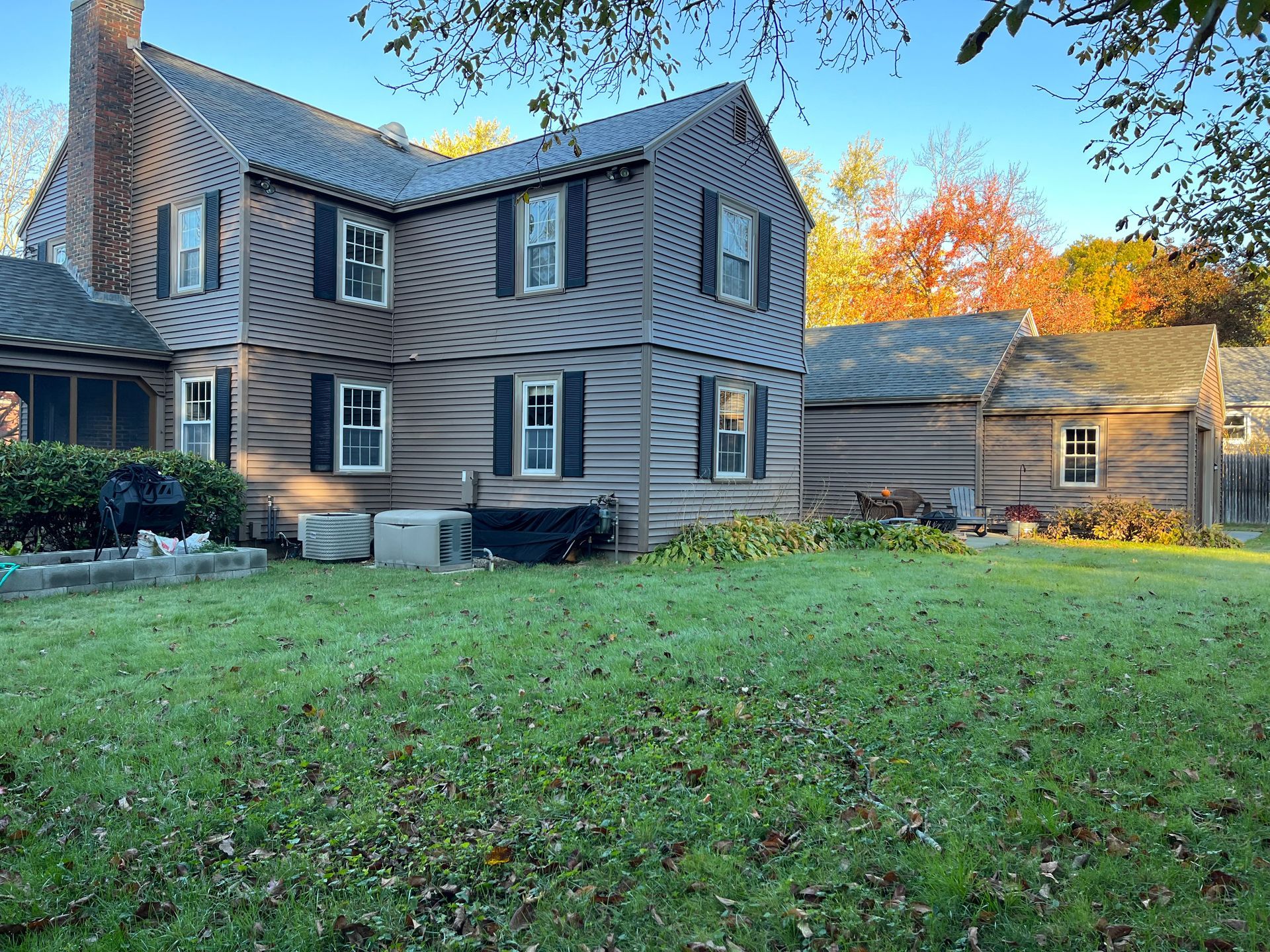 Gray two-story house with white trim and autumn trees behind a green lawn