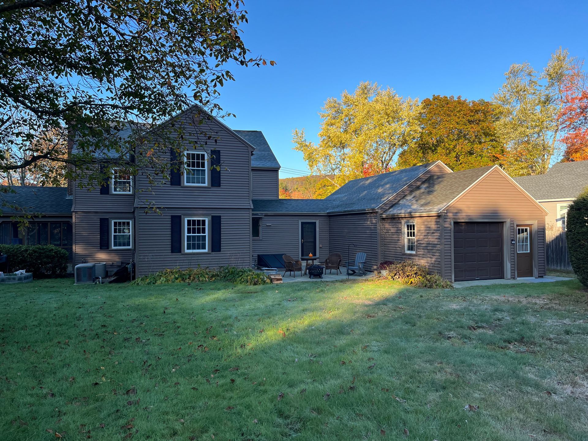 Suburban house with gray siding, attached garage, and sunlit autumn trees in the yard