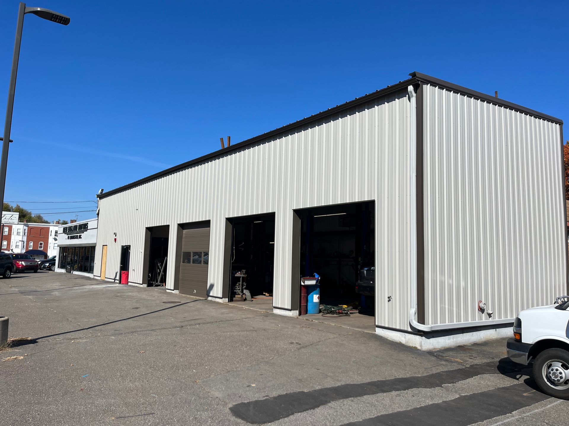 Industrial warehouse with open garage bays, white metal siding, and a blue sky overhead