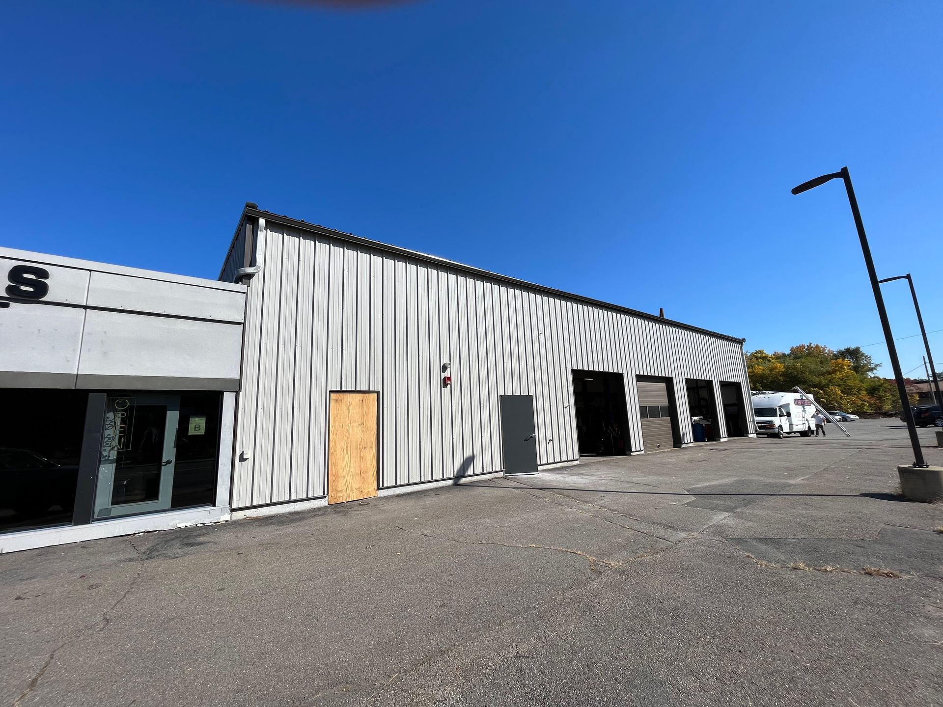 Empty strip mall storefront with corrugated metal facade and boarded door under a clear blue sky
