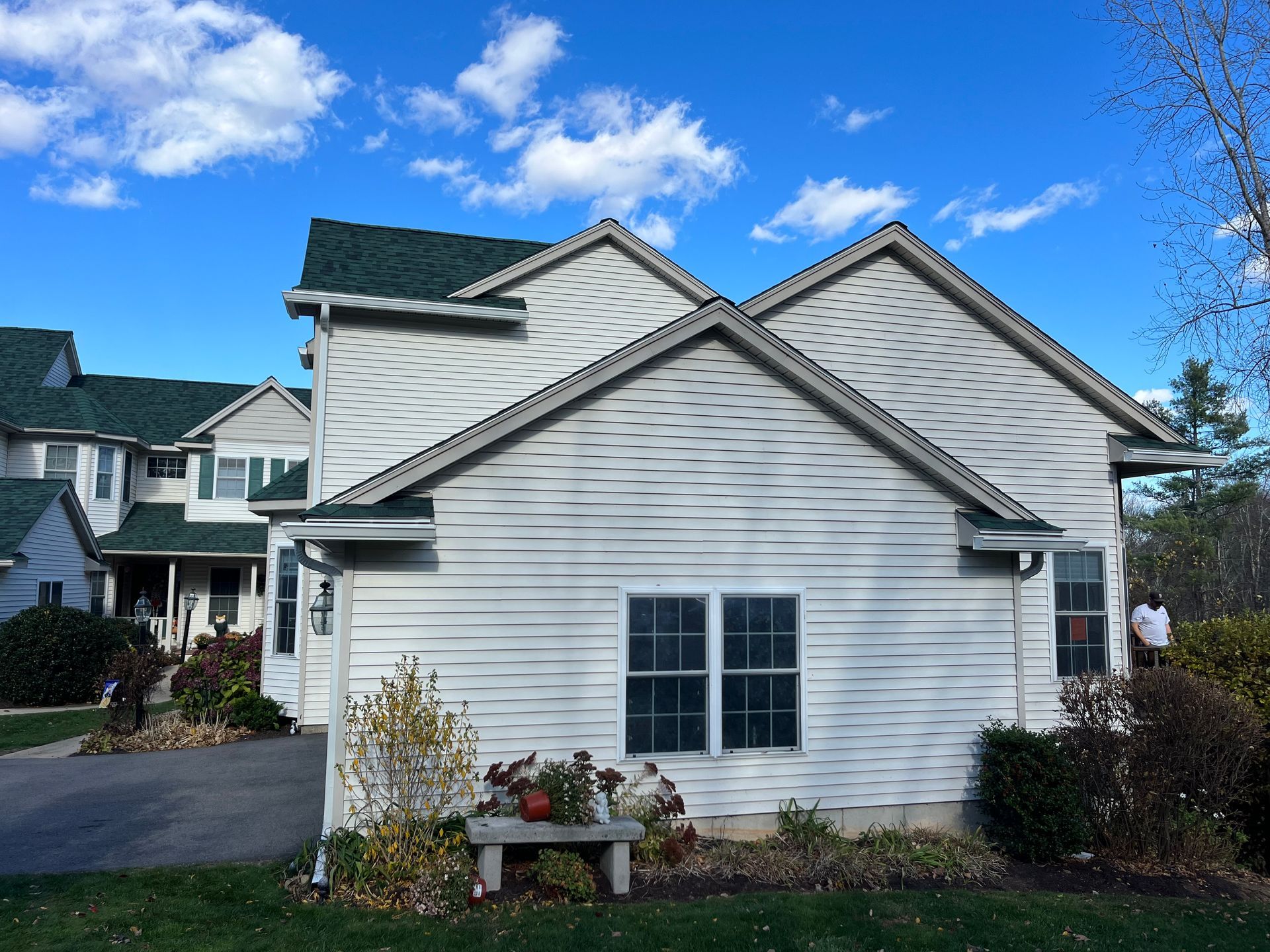 White suburban house with gray roof and front window, set beside a driveway under a bright blue sky