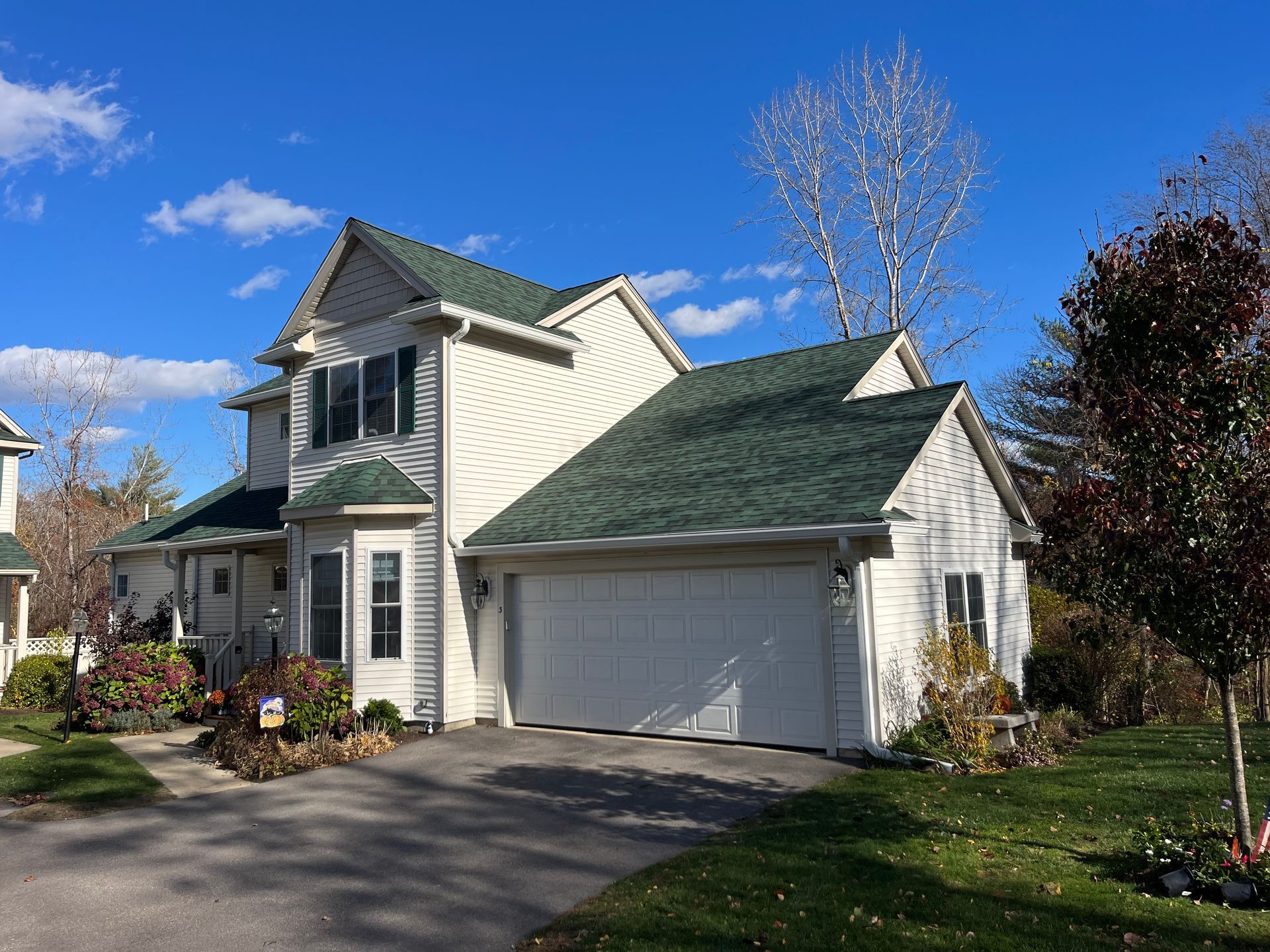Suburban house with green roof, white siding, garage, and landscaped front yard on a sunny day