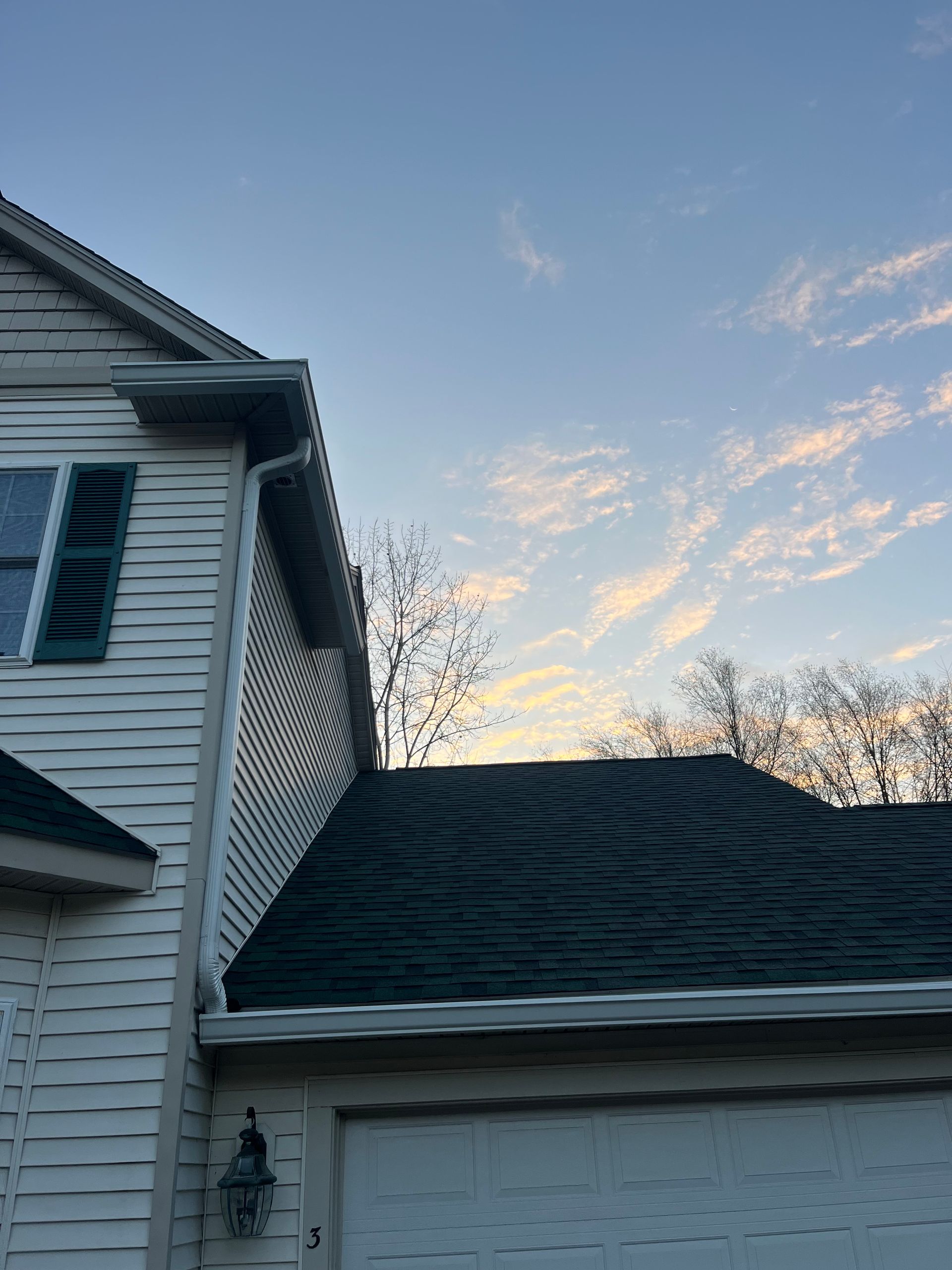 White house roof and siding at dusk, with a pale blue sky and wispy sunset clouds.