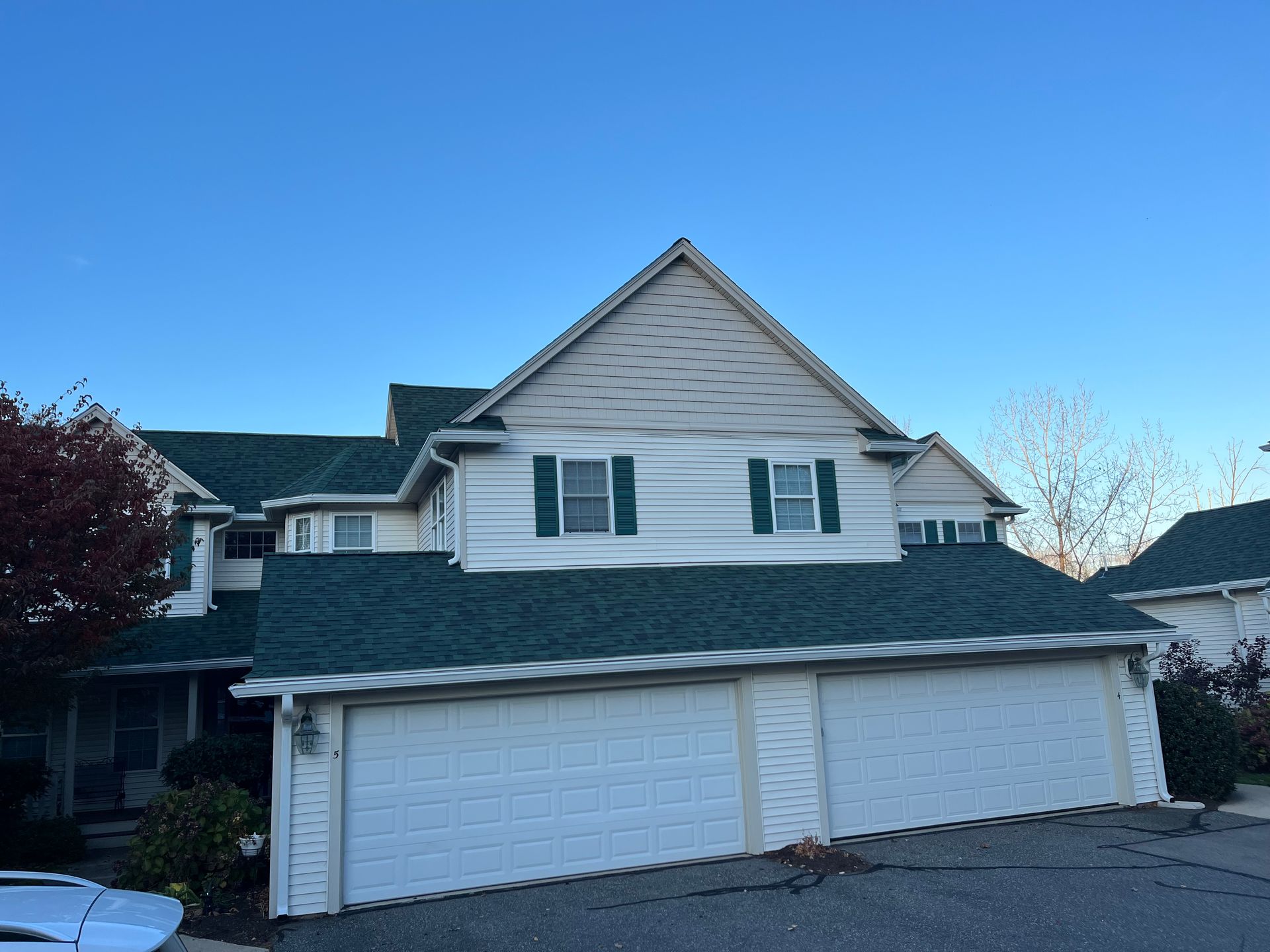 Suburban two-story house with white siding, green roof, and a three-car garage under a clear blue sky