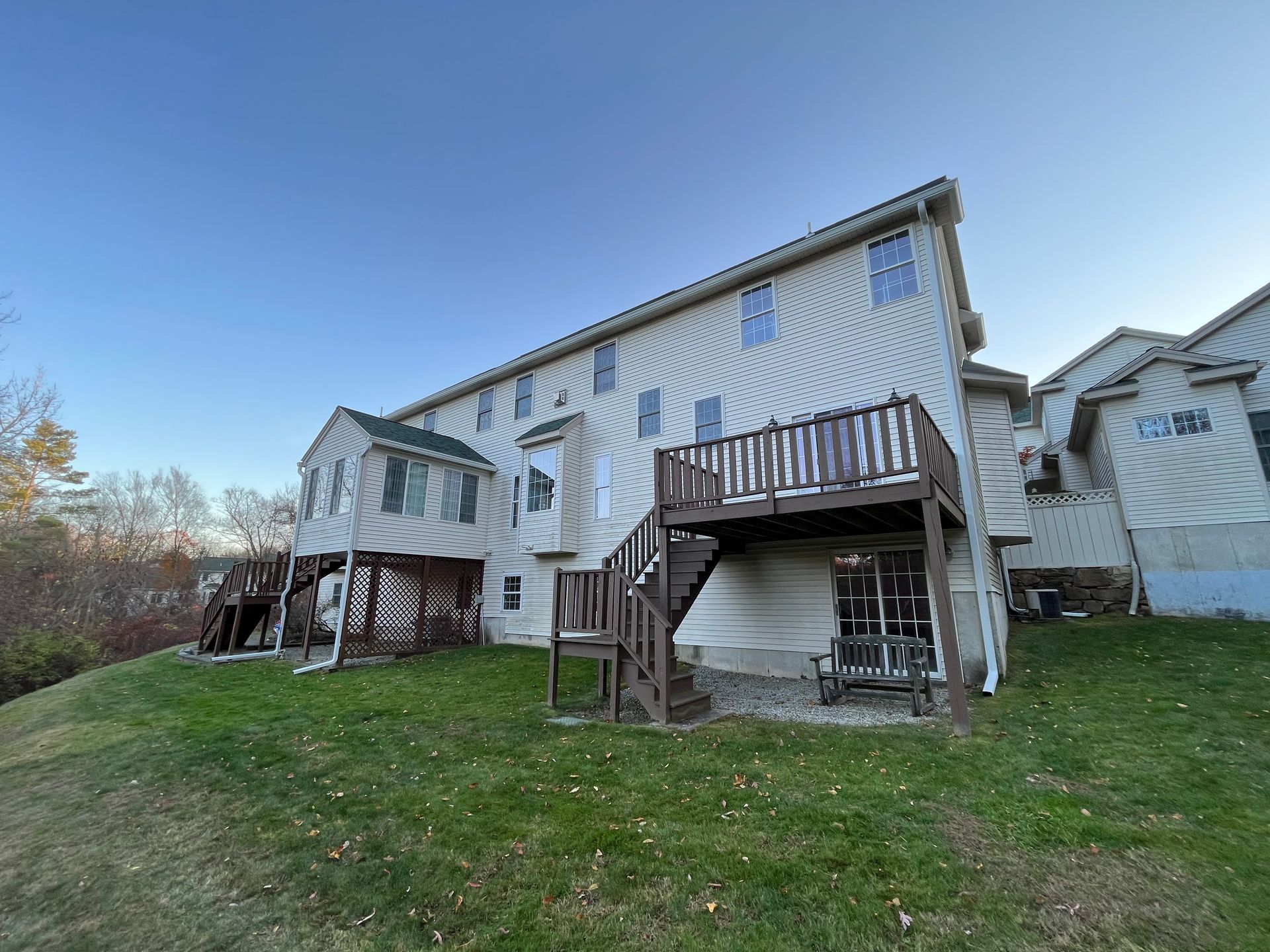 Rear view of a white multi-level house with decks, stairs, and a grassy backyard under a clear sky