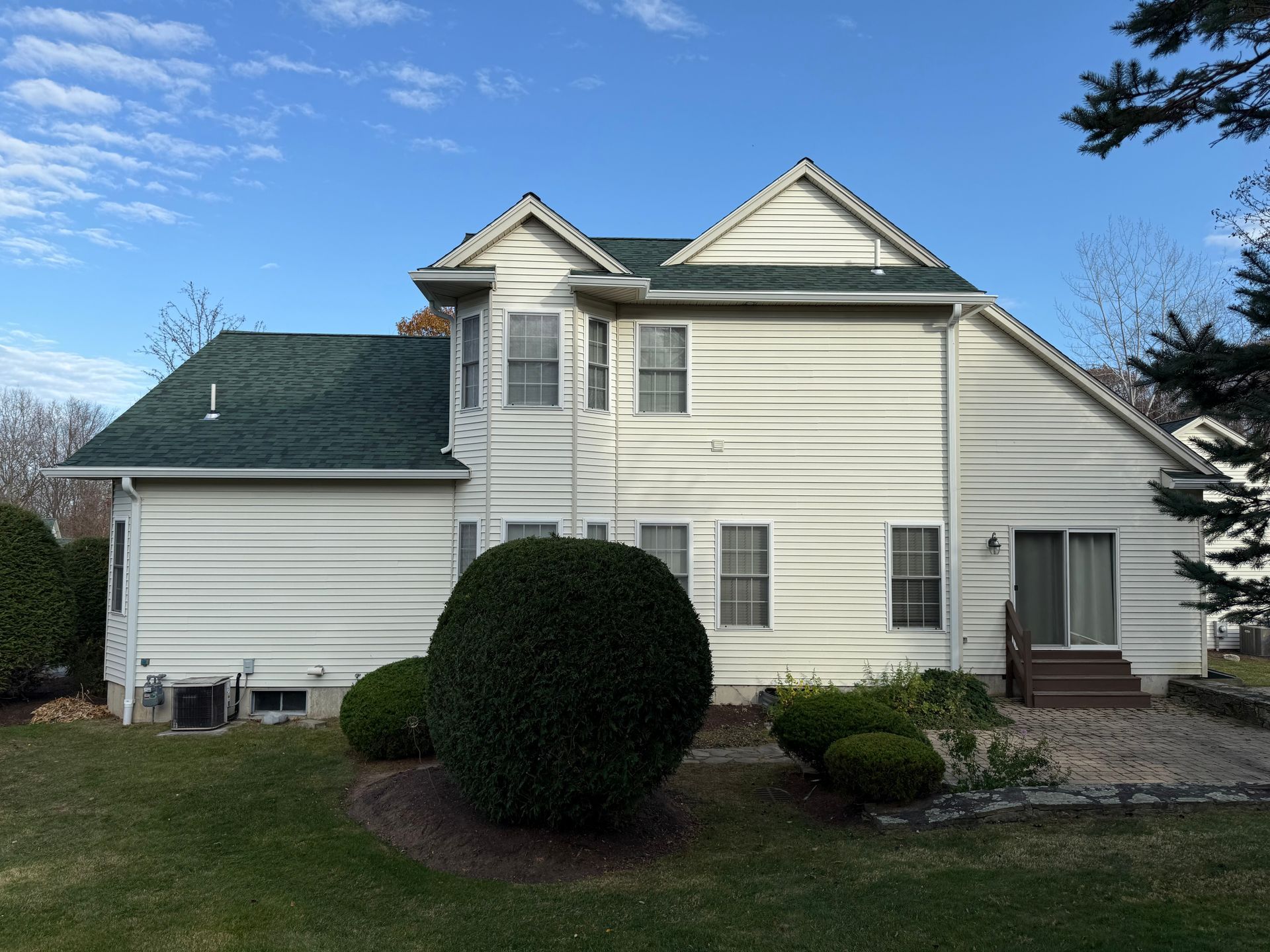 White two-story house with green roof, dormer windows, and a front shrub under a blue sky