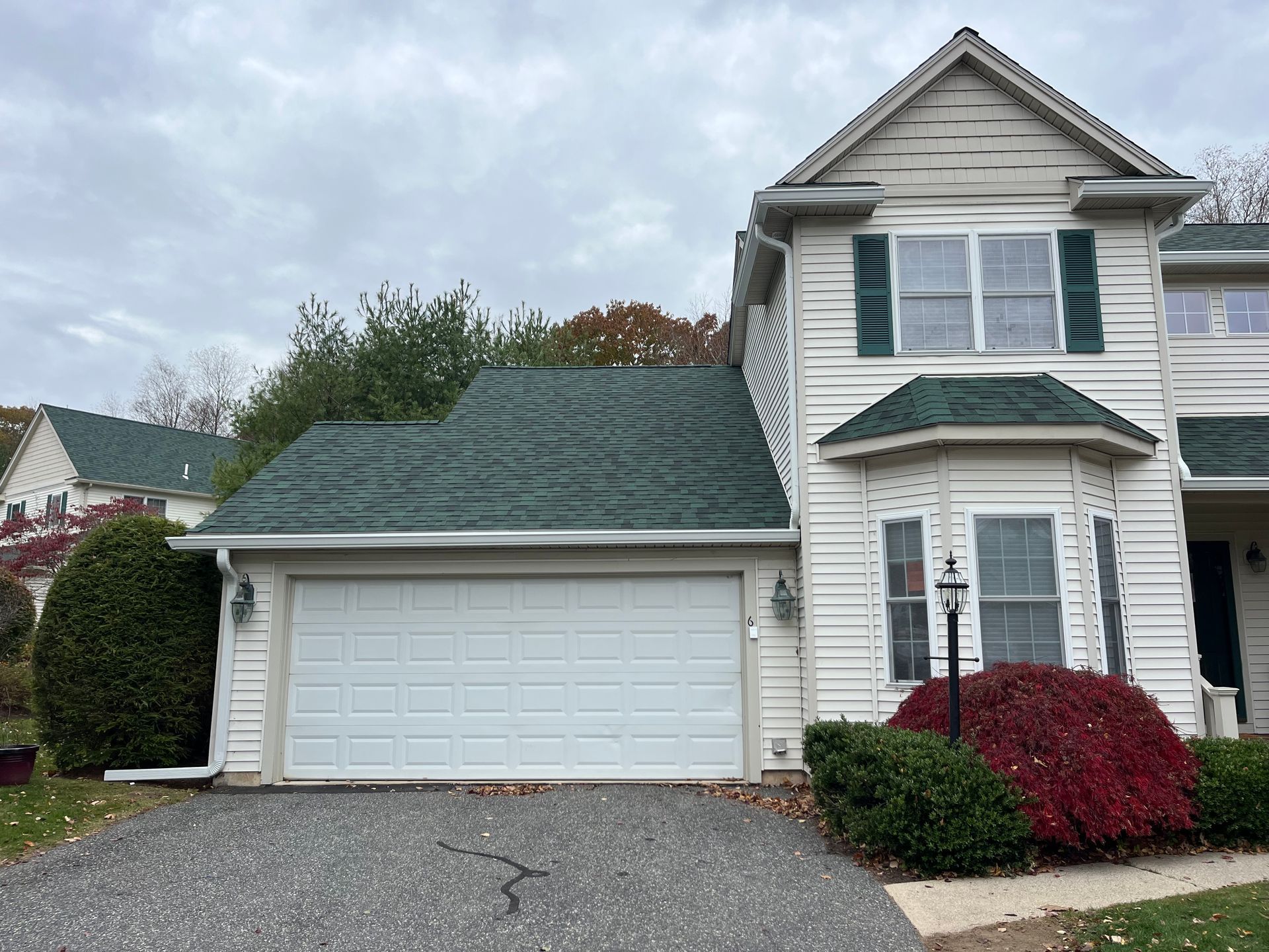 Suburban two-story house with white siding, green roof, attached garage, and red shrubs in front