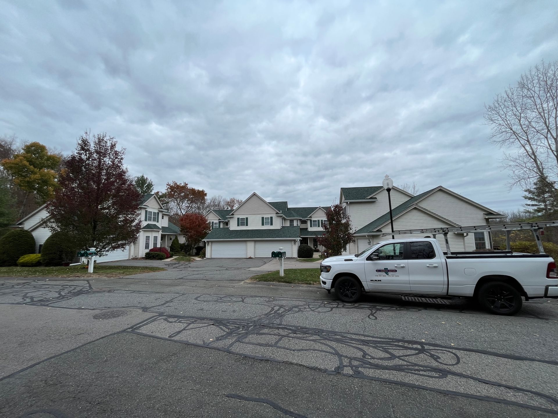 White pickup truck parked on a cracked suburban street under a cloudy sky, with houses and trees nearby