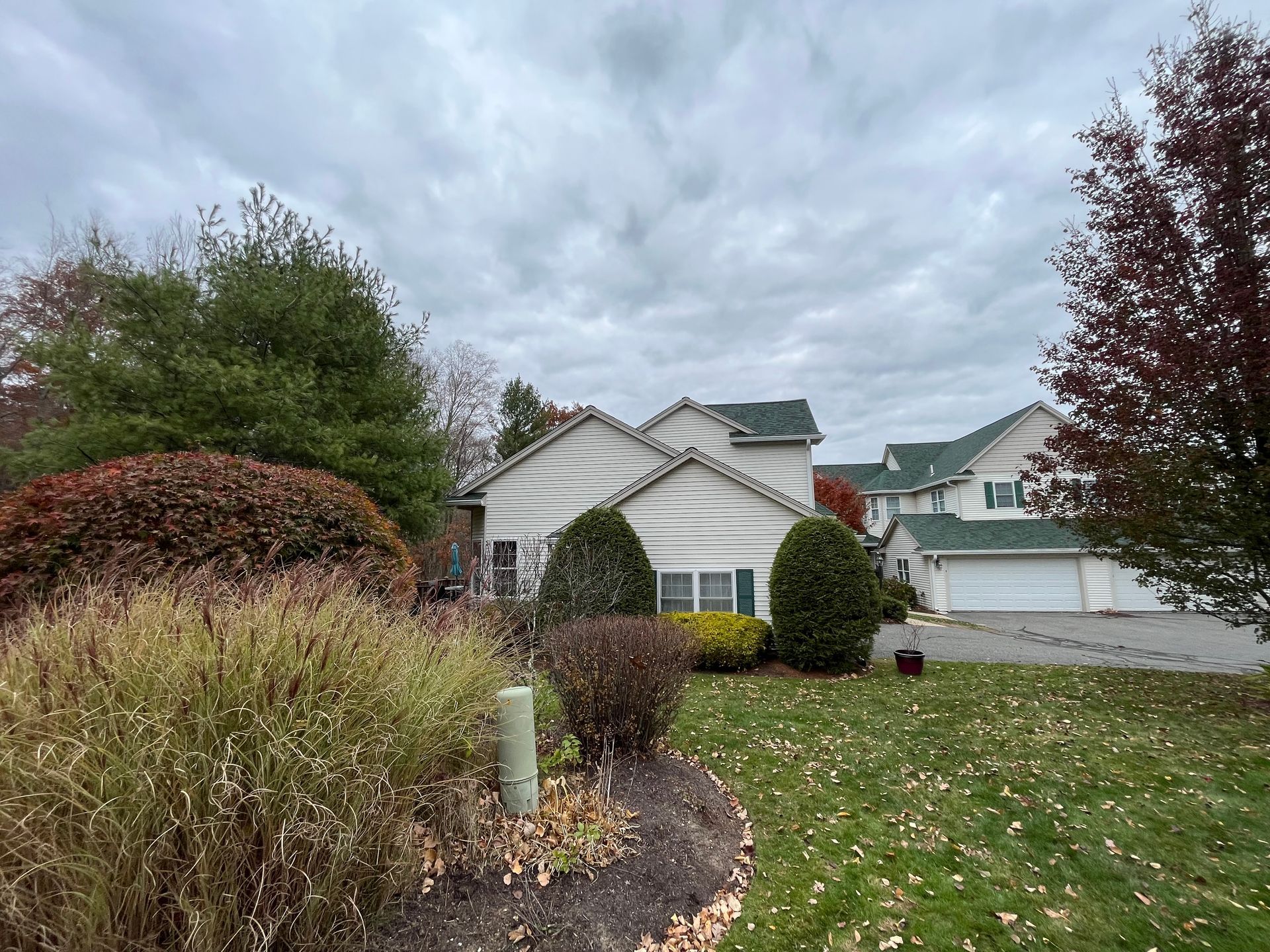 Suburban house with white siding, green lawn, autumn shrubs, and cloudy sky