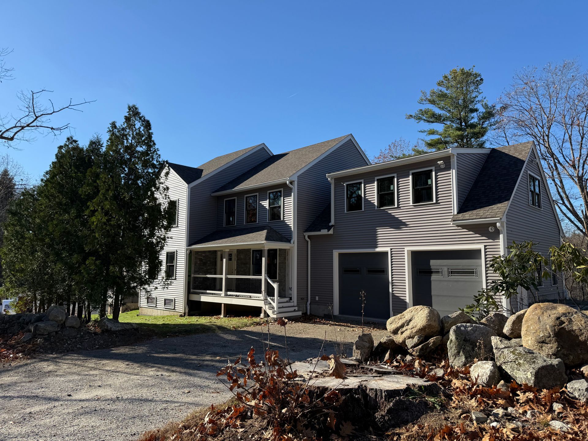 Two-story gray house with porch, garage, and rock landscaping under a clear blue sky