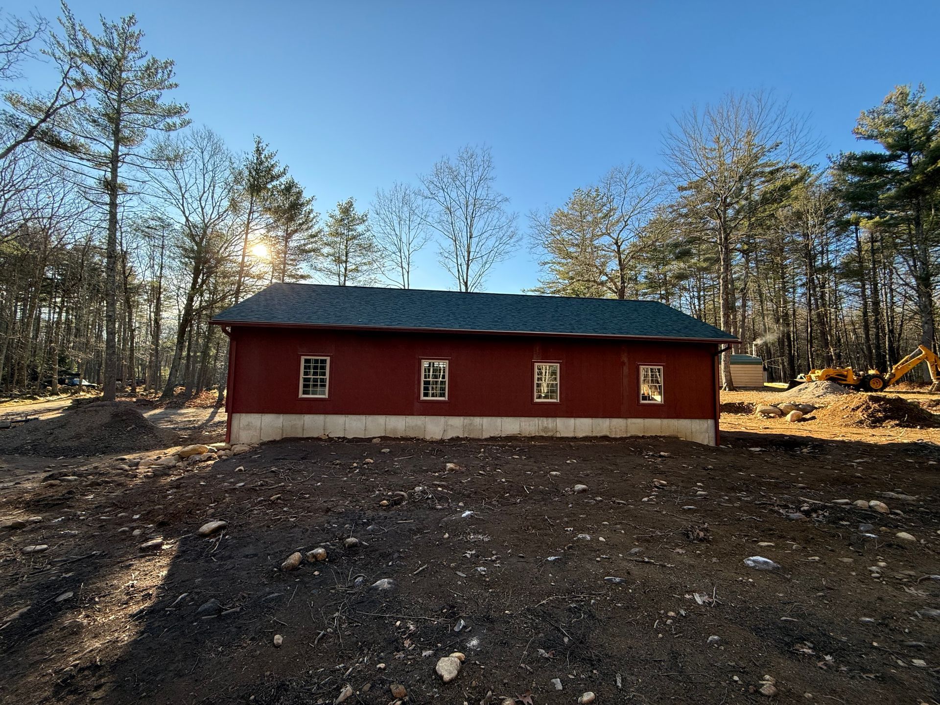 Red barn-style building with a dark roof in a clearing among trees under a blue sky