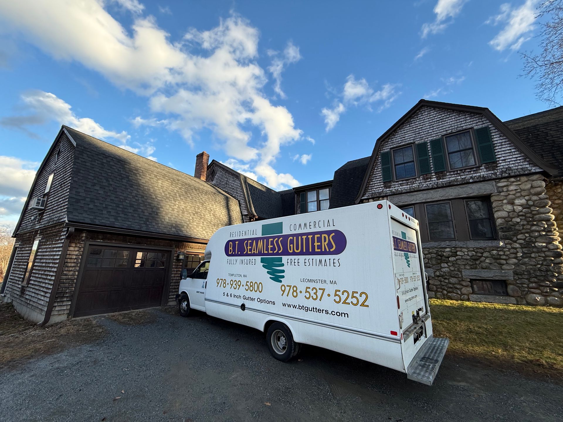 White utility van parked beside rustic stone buildings under a blue sky with clouds