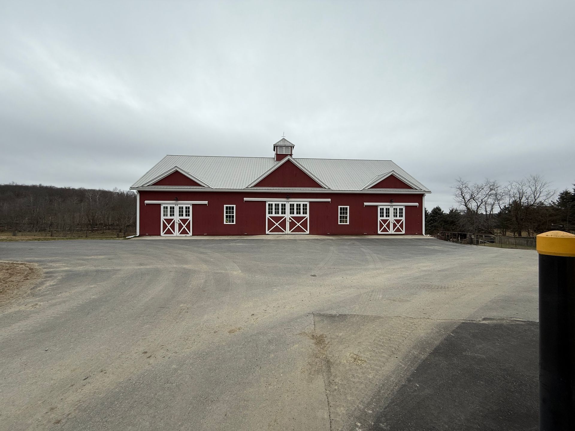 Red barn-like building with white trim on a gravel lot under an overcast sky