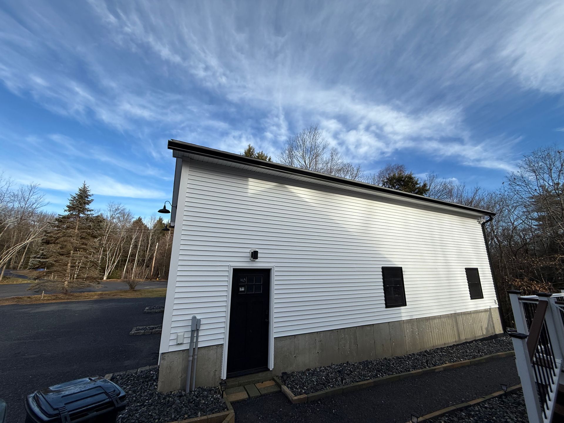 White utility building with black door and windows under a blue, cloud-streaked sky