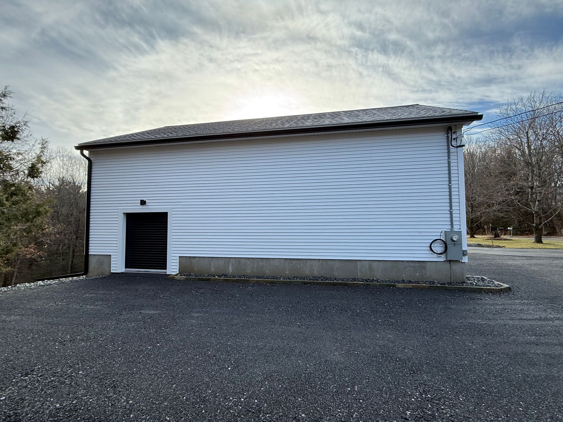 White metal-sided building with a small side door, set on a gravel lot under a cloudy sky