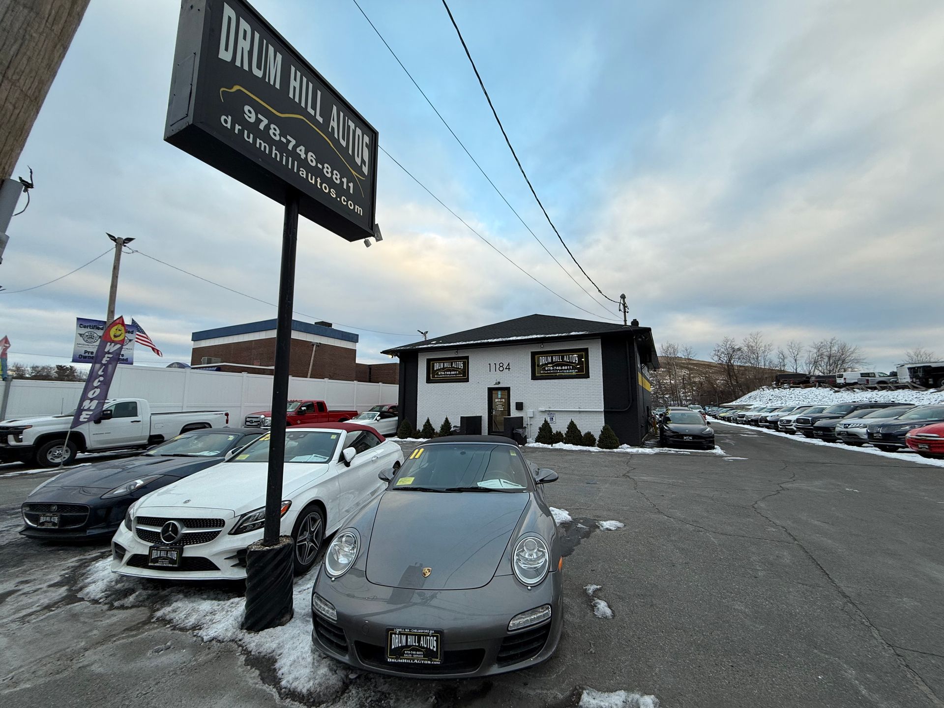 Parking lot with a black sports car, a white sedan, and a black storefront under a cloudy sky.