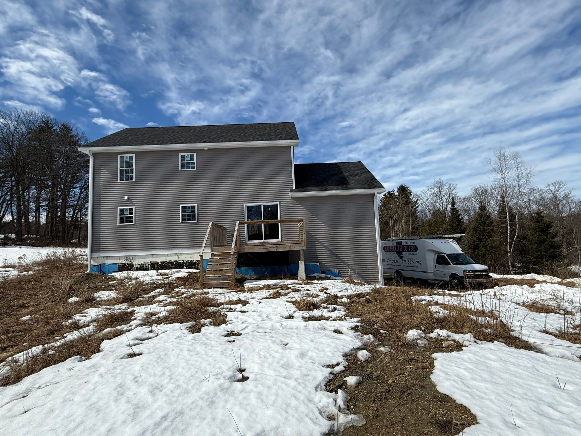 House under construction on a snowy hillside, with blue siding, solar panels, and a white van nearby.