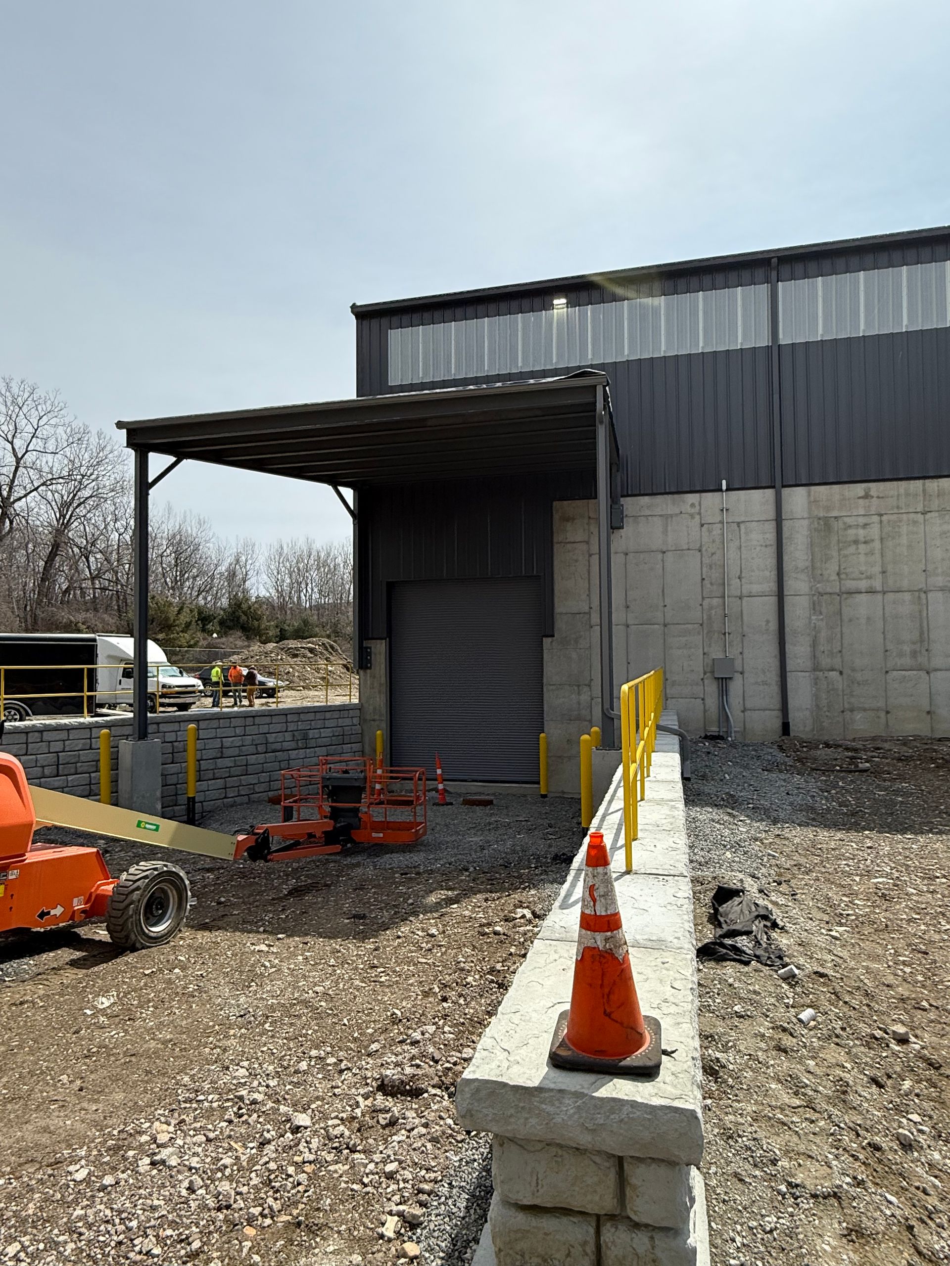 Industrial building exterior with metal siding, orange cones, and equipment on a gravel lot