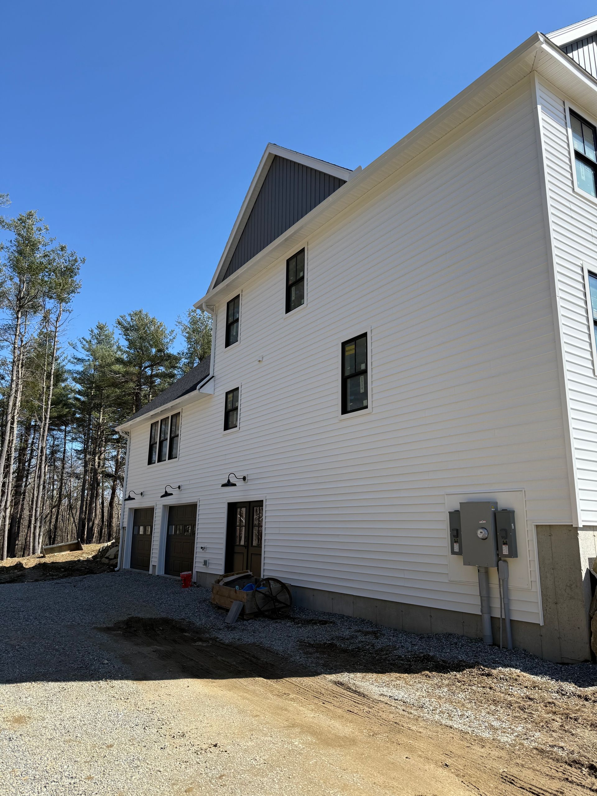 White multi-story house with black-trimmed windows and a gravel yard under a blue sky