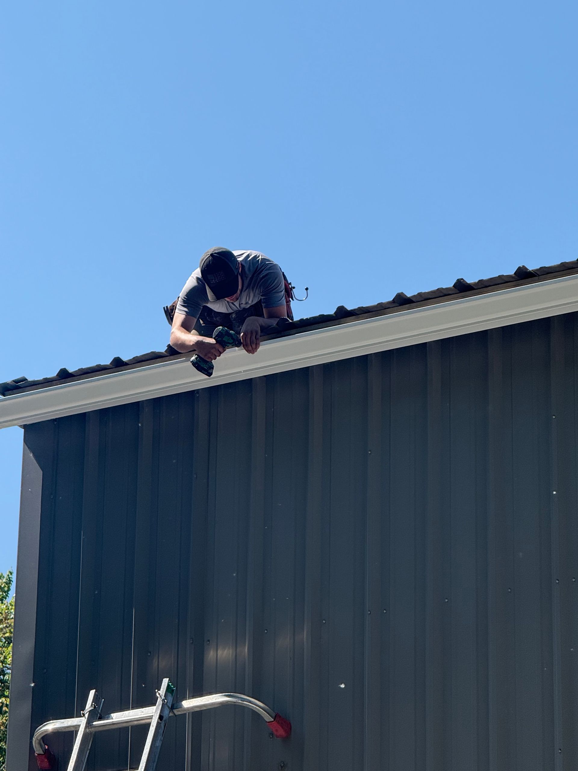 Person crouching on a roof edge above a blue building under a clear sky