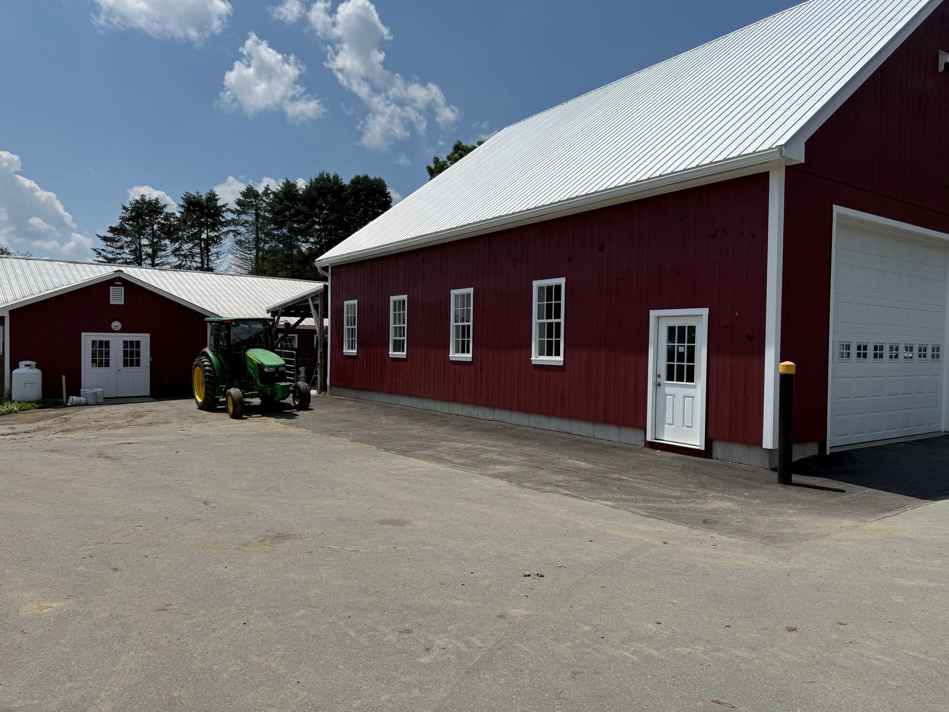 Red barn-style buildings with white roofs and a green tractor in a gravel farmyard