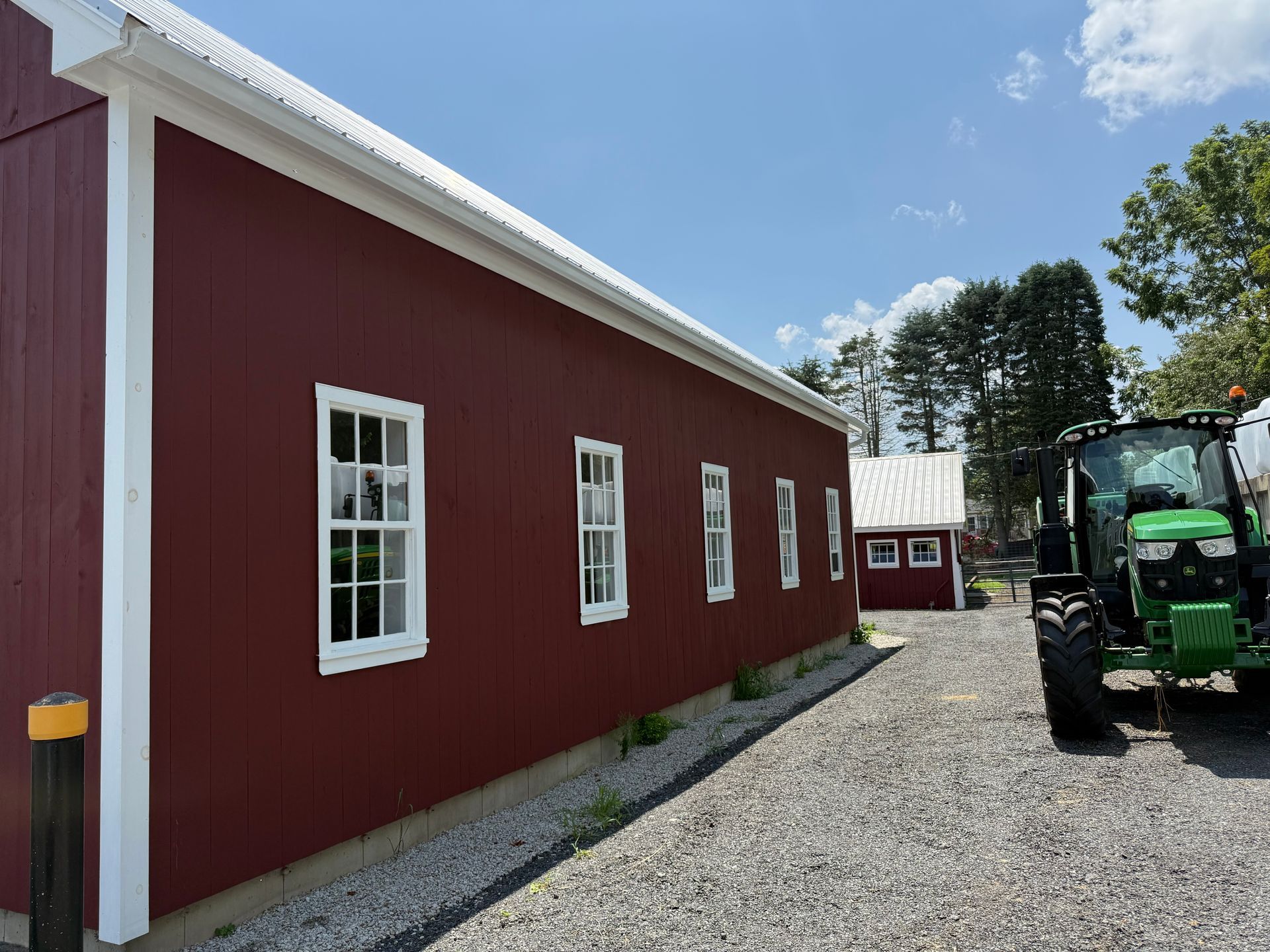 Red barn-style building with white trim along a gravel drive, with a green tractor parked beside it.
