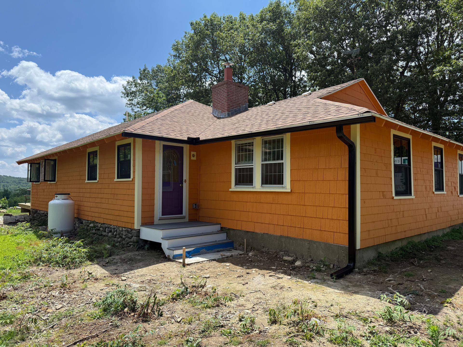 Single-story orange house with a brown roof and small front steps under a blue sky