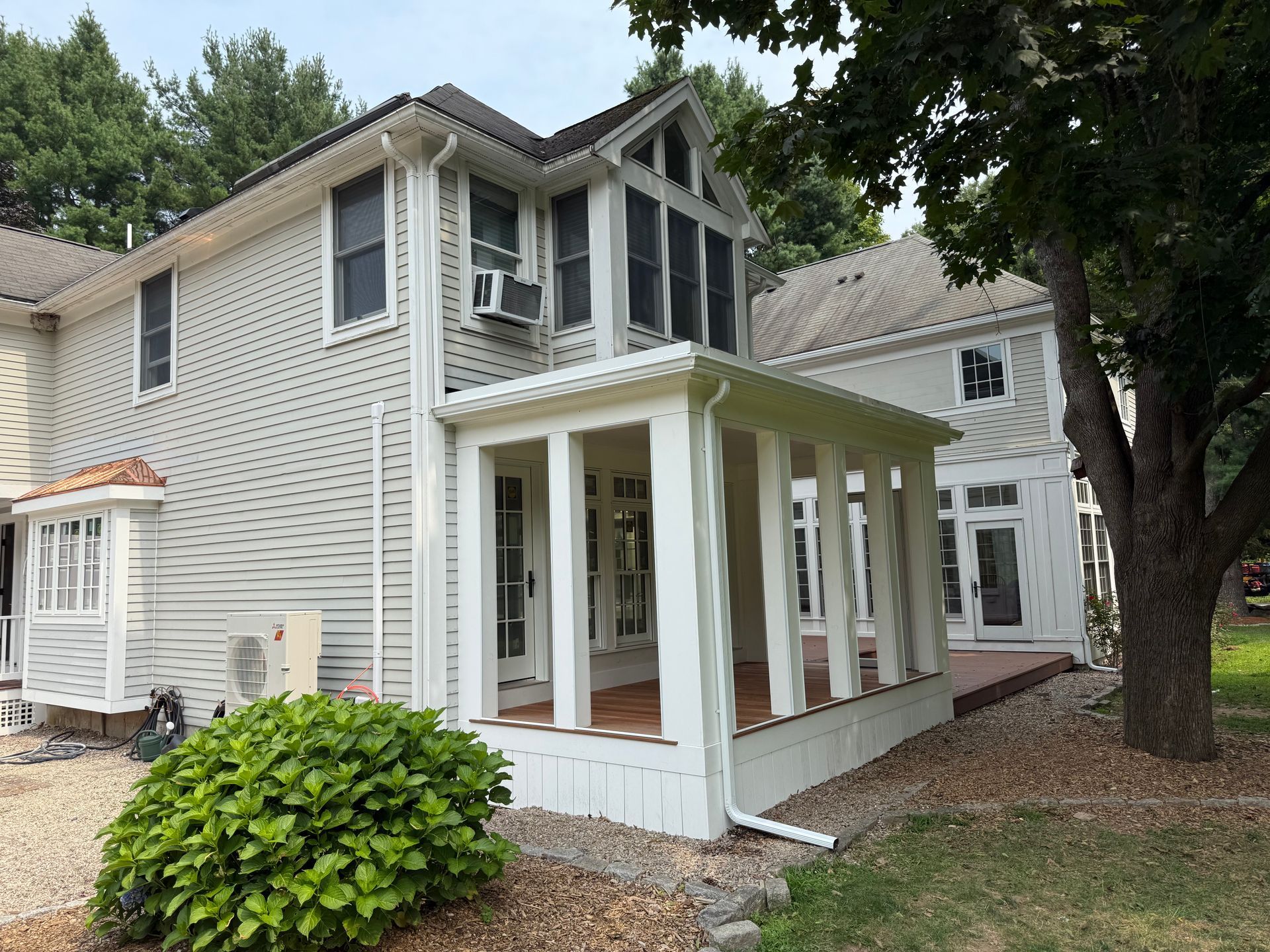 White two-story house with screened porch, dark roof, and large tree in front yard
