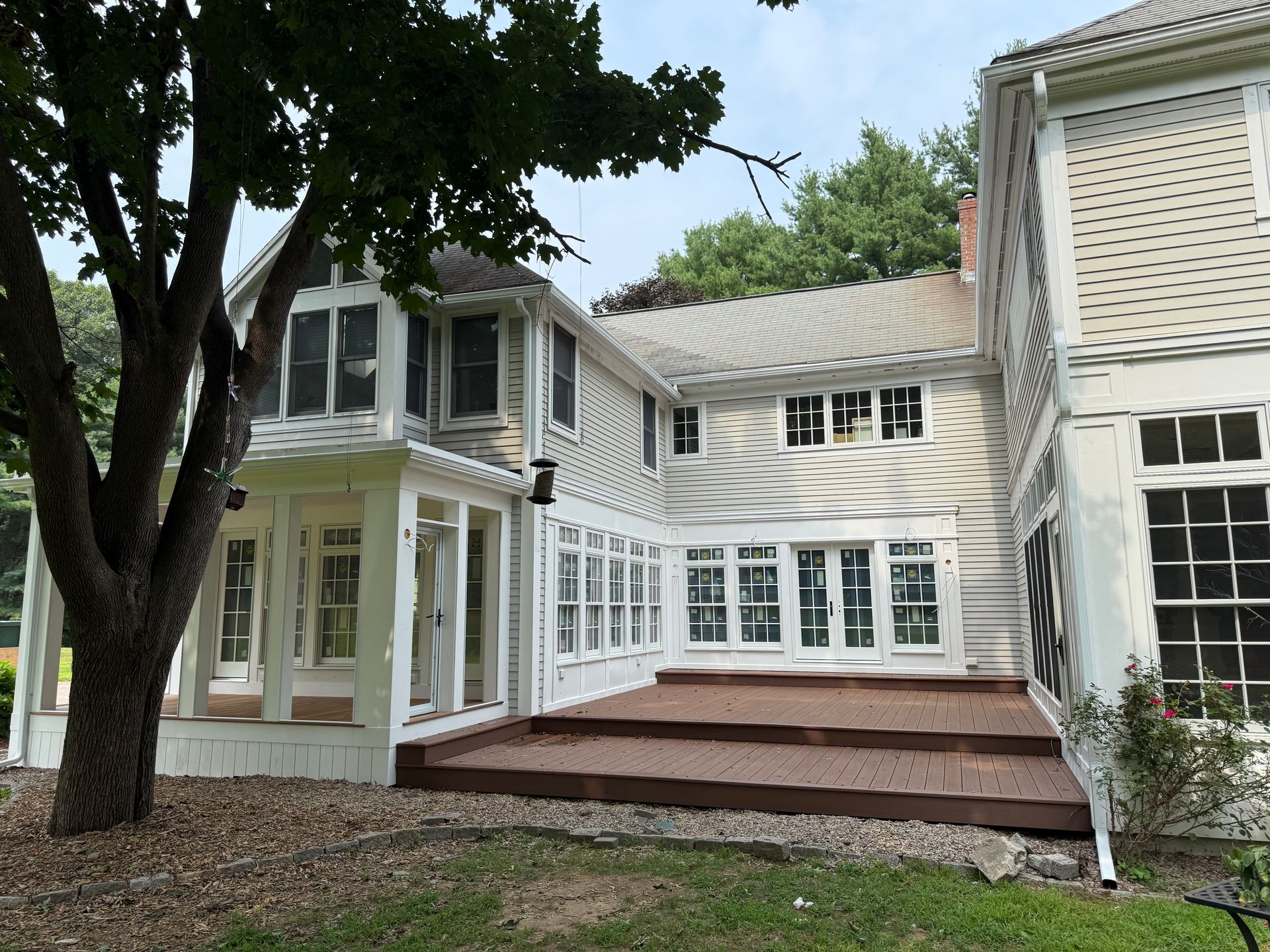 White two-story house with large windows, porch, and wooden deck under trees