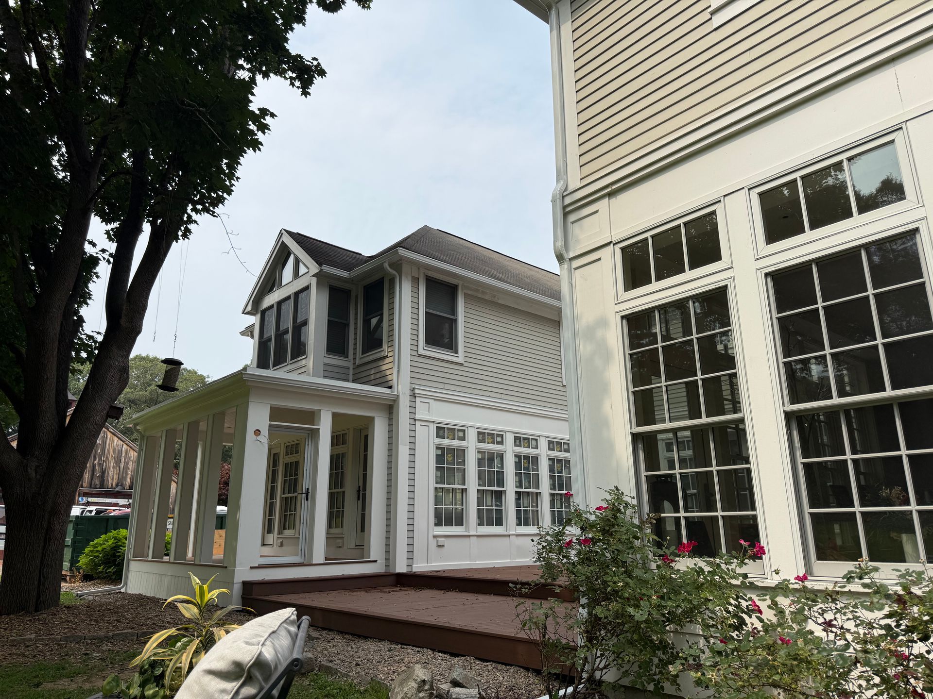 White house porch with large windows, trees, and a small garden in front