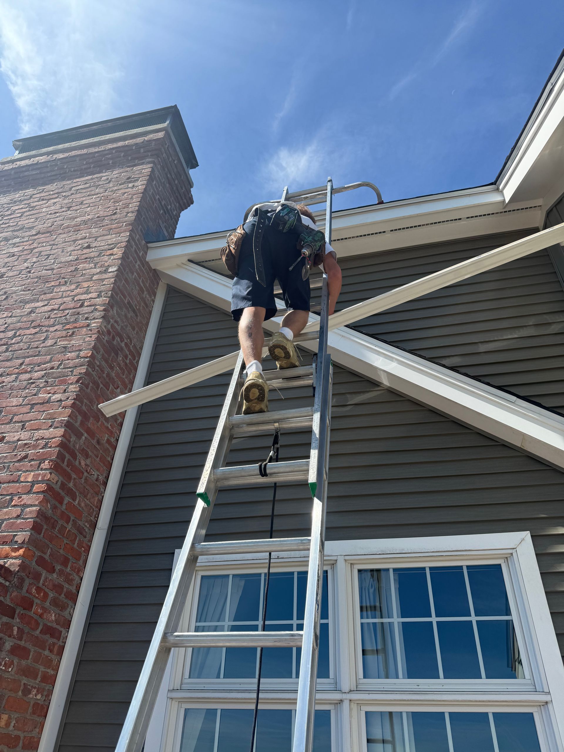 Worker on a ladder repairing the roof of a house beside a brick chimney