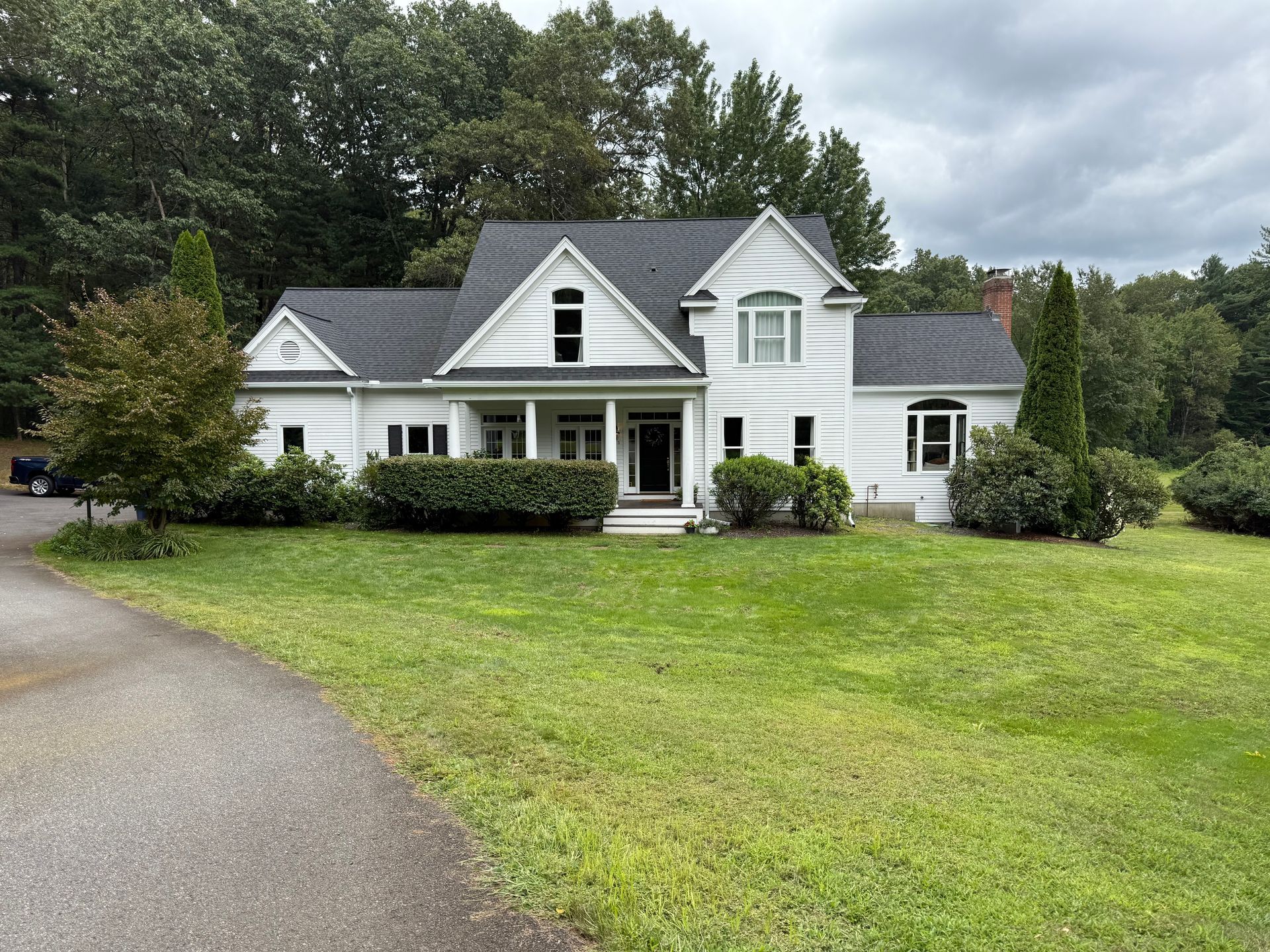 White house with black roof and front porch, set in a green lawn beside a curved driveway.