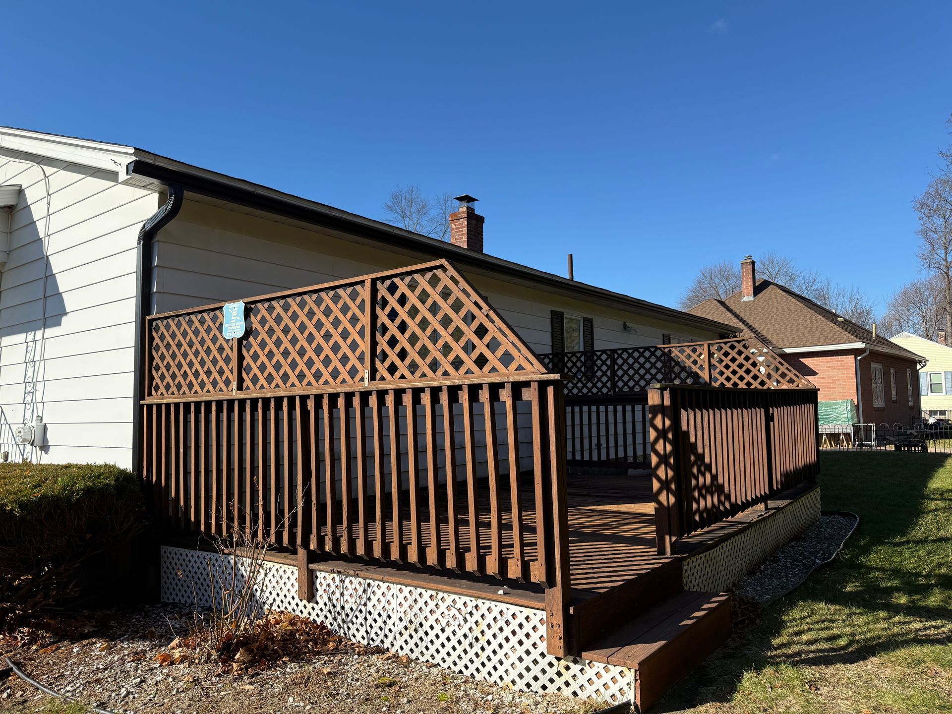 Wooden front porch deck with brown lattice railing beside a house on a sunny day