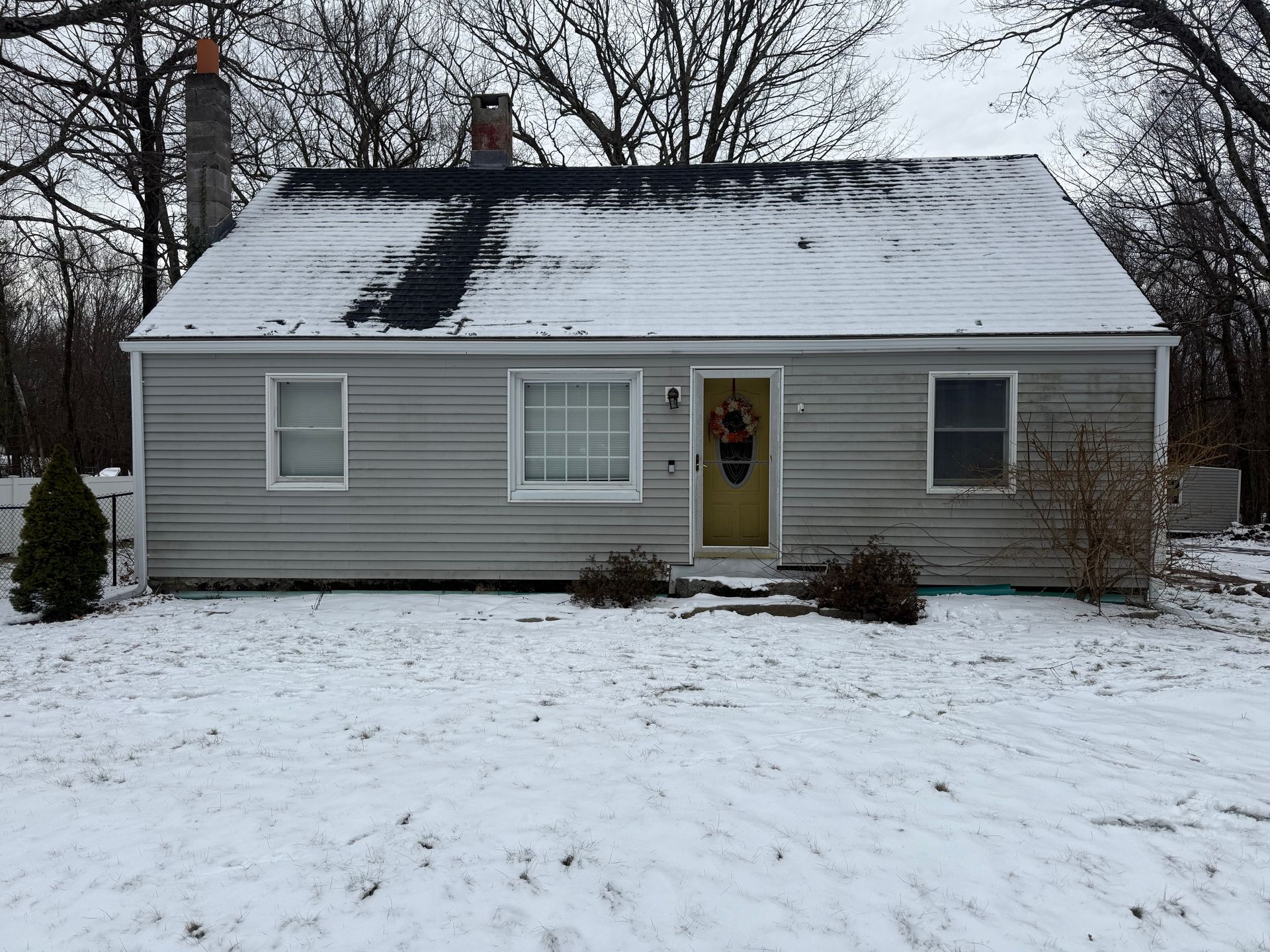 Small gray house with a snow-covered roof and yard in winter.