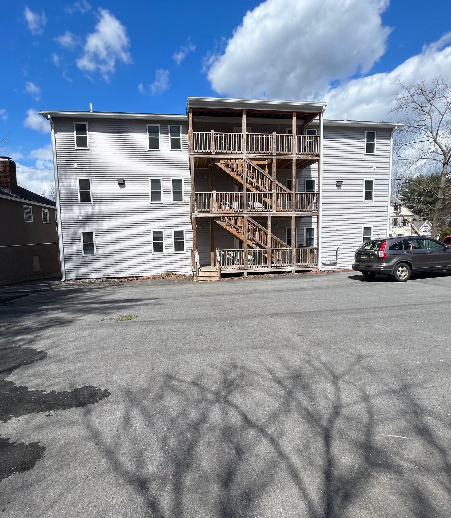 Partially renovated white apartment building with exposed wooden stairways and a parked car in front