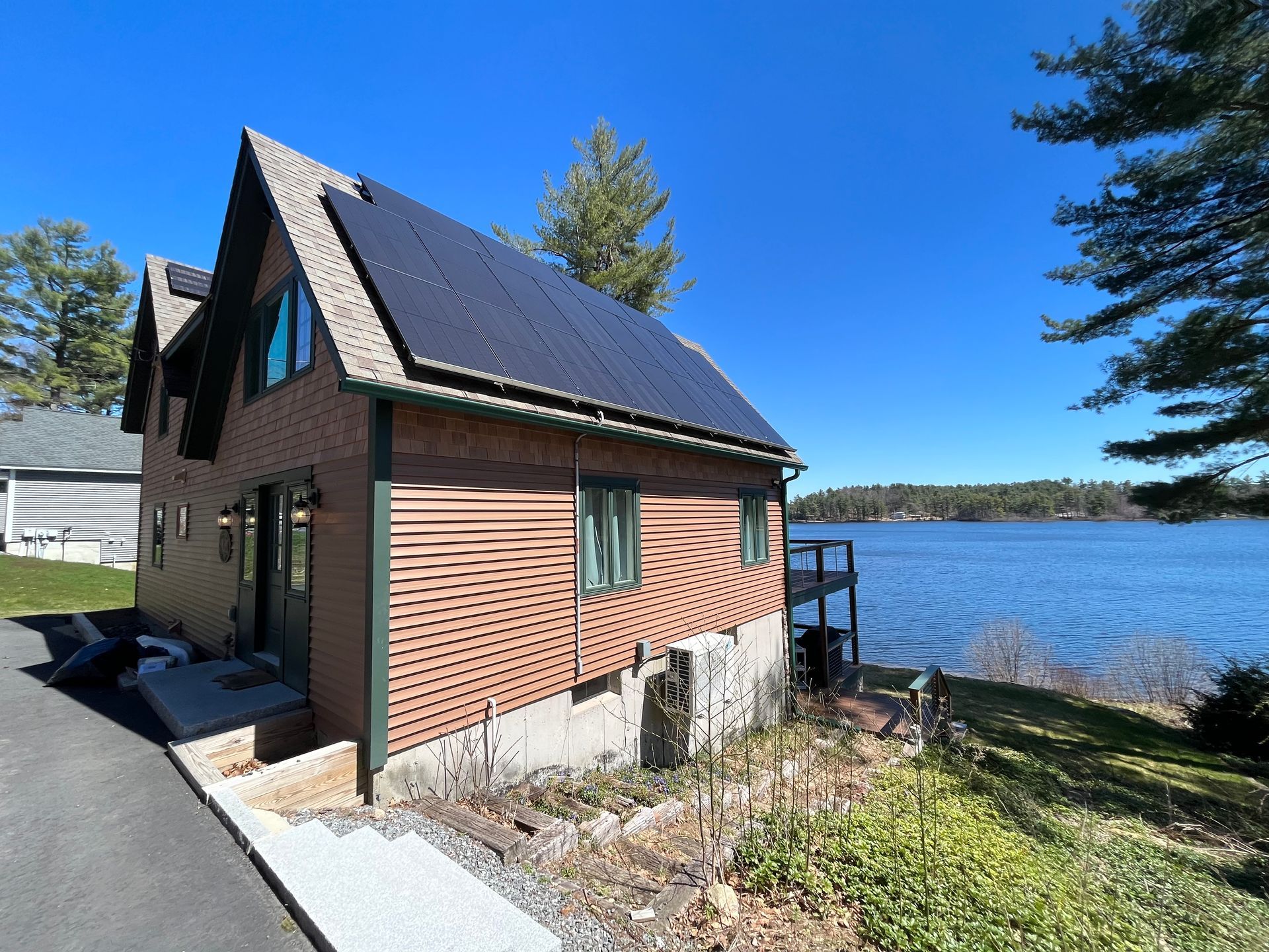 Small lakeside cabin with dark roof and red siding beside a road under a clear blue sky