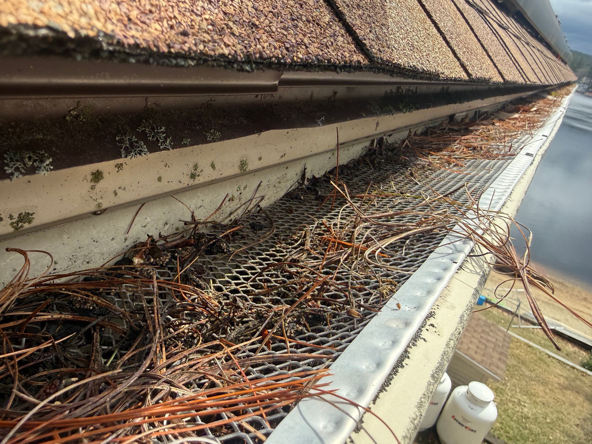 Clogged roof gutter packed with leaves, twigs, and debris beside a house roofline