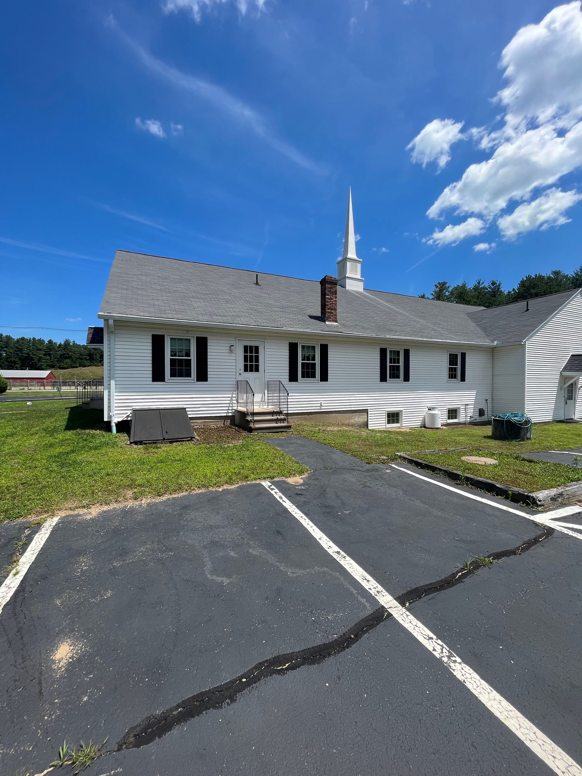 White church building with a tall steeple beside a parking lot under a bright blue sky