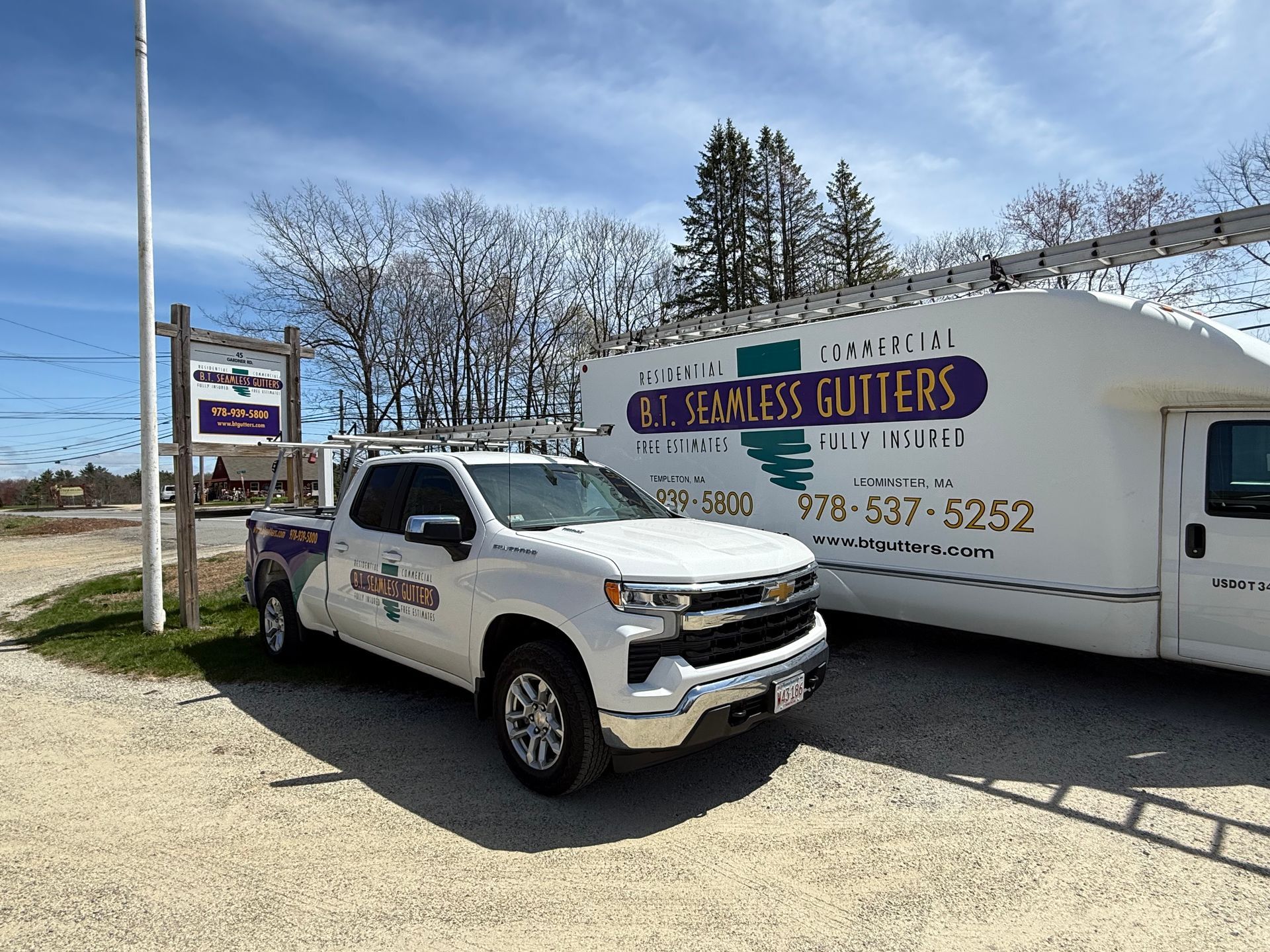 White service truck parked beside a trailer with “J.R. Gutter Gutter” signage on a sunny roadside lot
