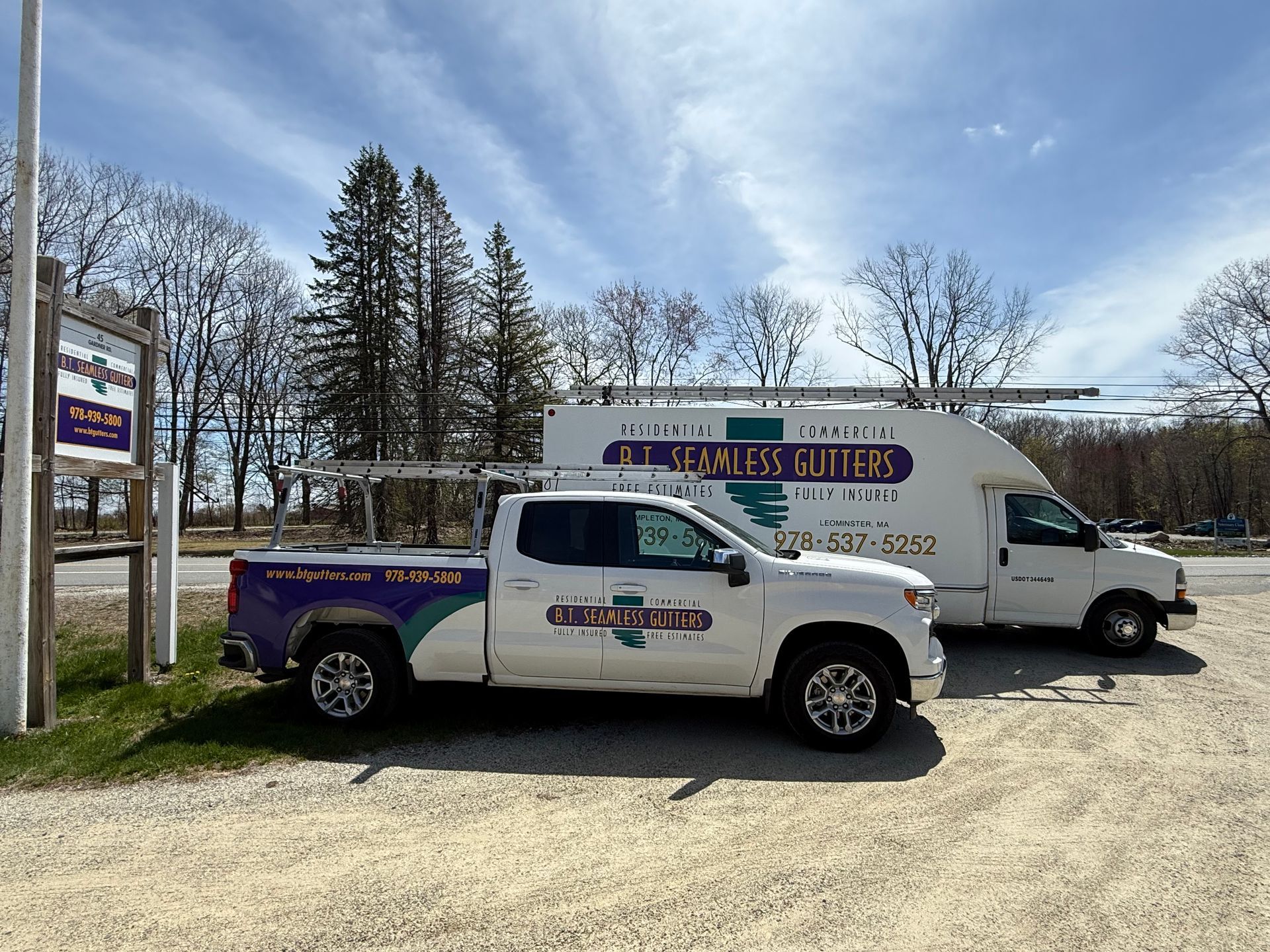 Two service trucks parked outdoors, one white with purple branding and one white van, under a cloudy sky.